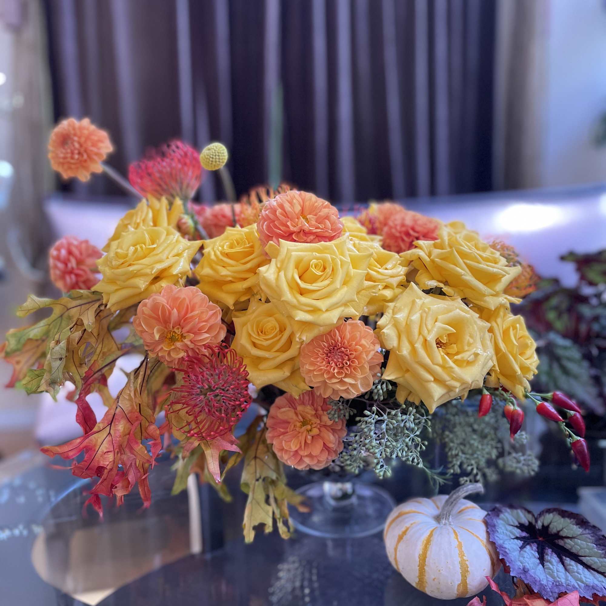 Yellow roses and orange dahlias in a low arrangement with autumn leaves