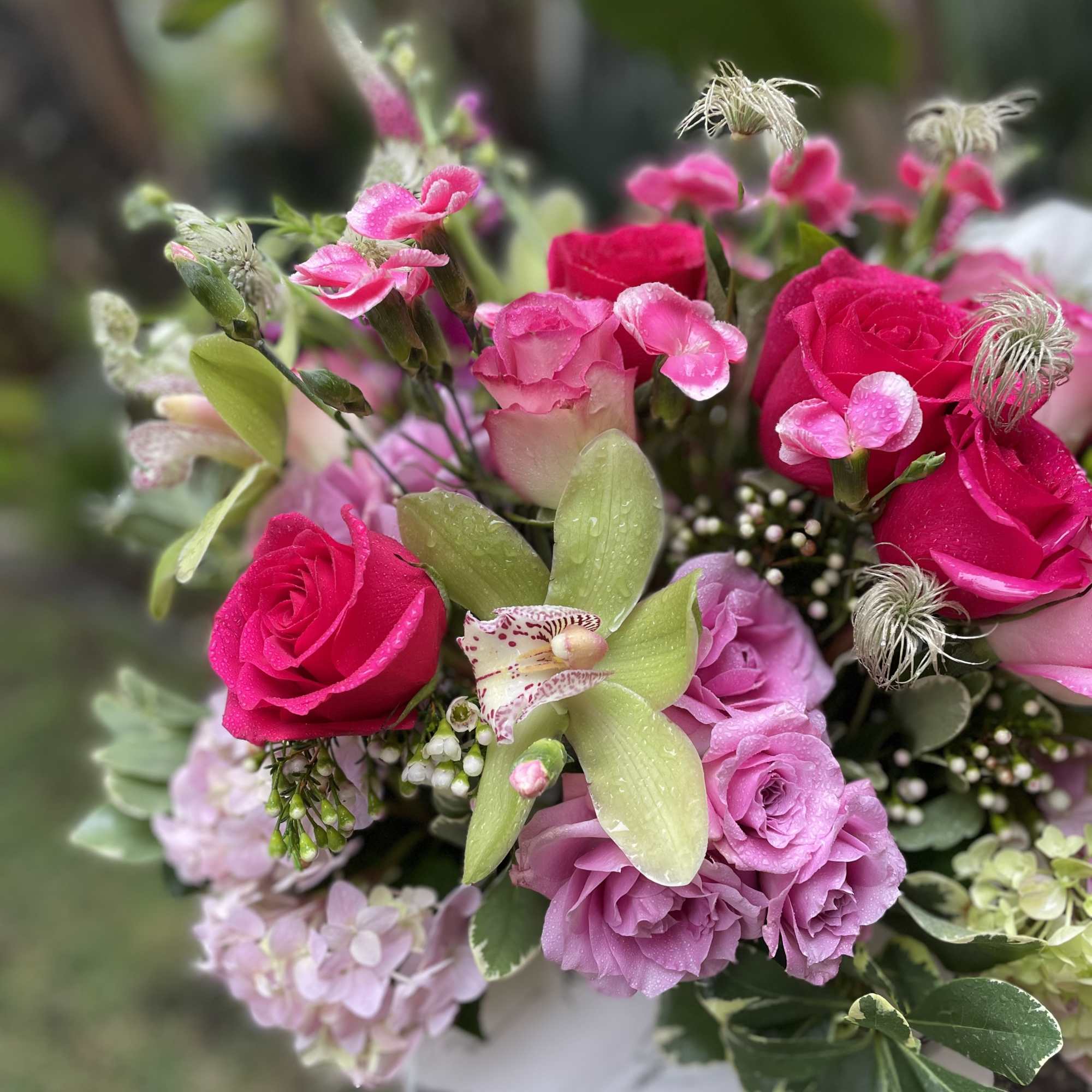 Bouquet of pink roses, orchids, and hydrangea in a white wrap