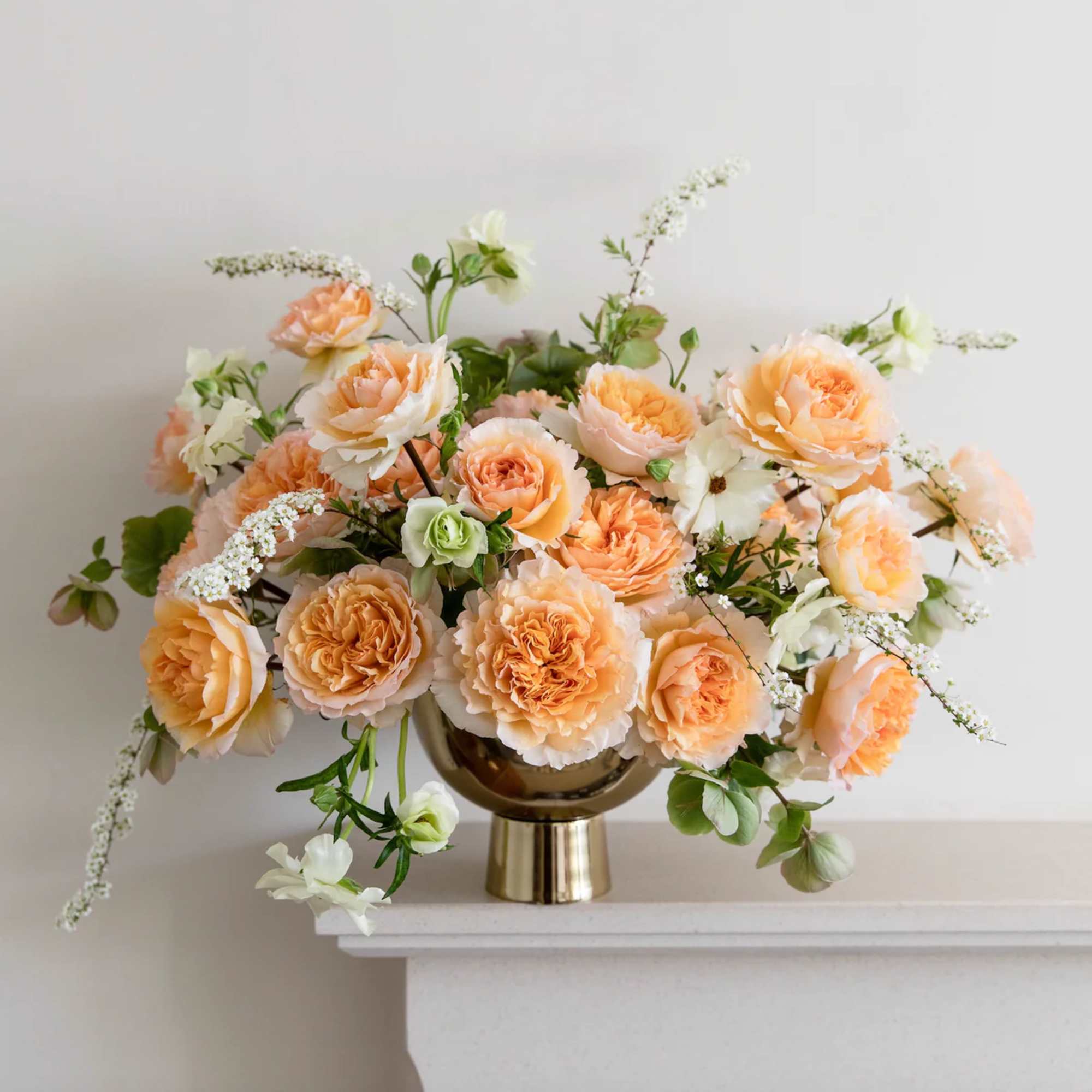 Peach and white roses arranged in a gold vase