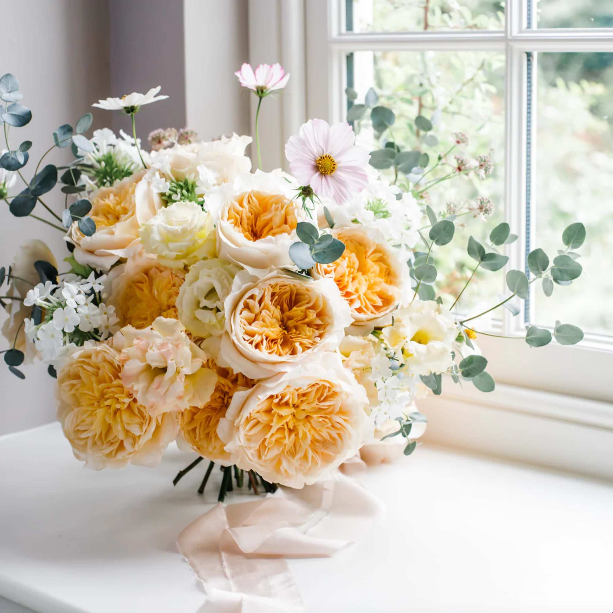 Bouquet of peach and white roses with airy greenery on a ribbon-tied stem