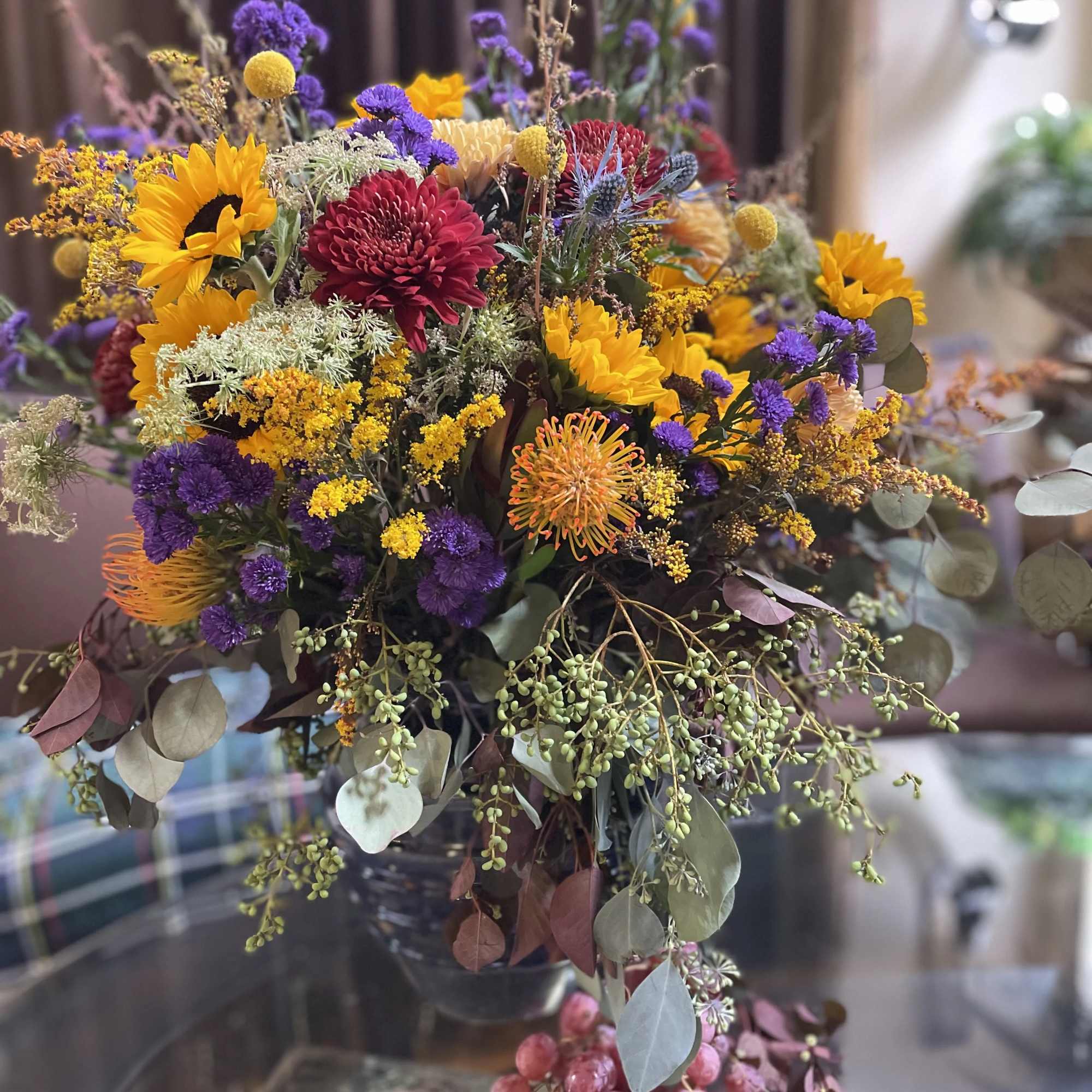 Mixed bouquet with sunflowers, chrysanthemums, and purple filler flowers in a glass vase