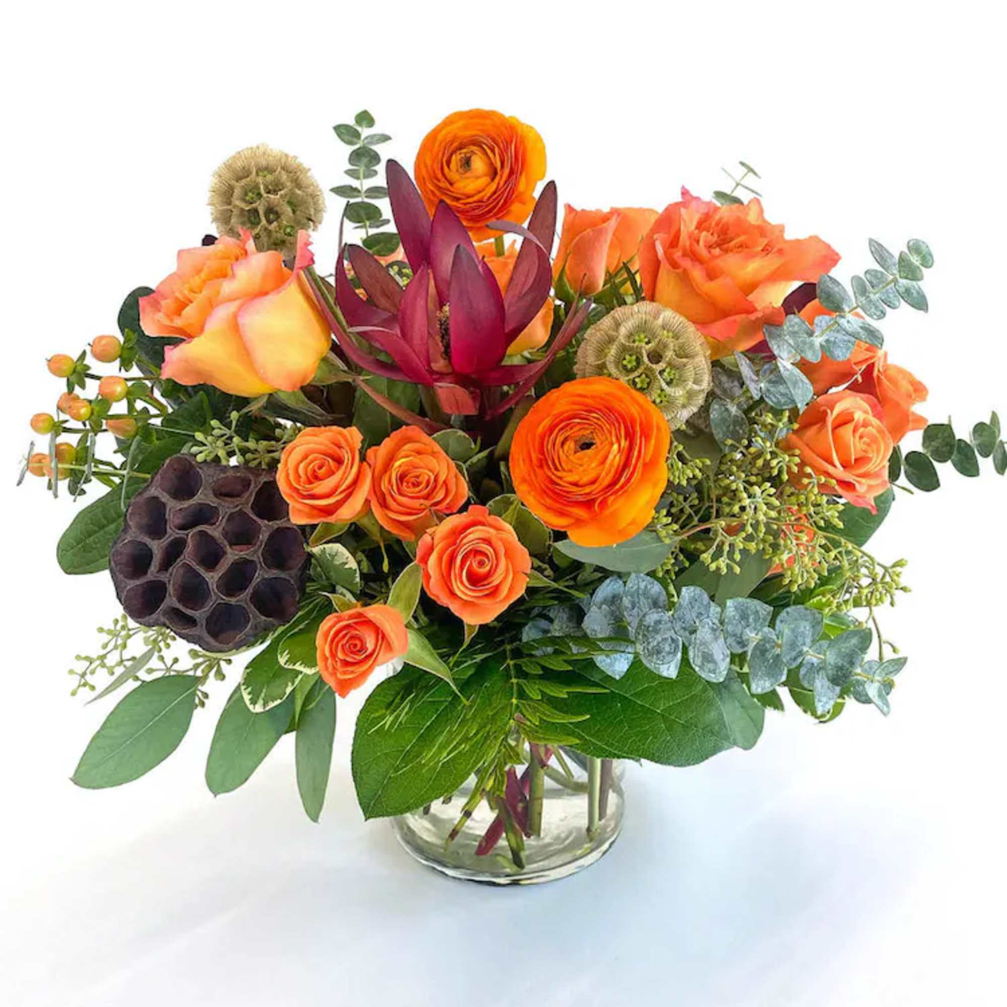 Orange roses and ranunculus in a glass vase with mixed greenery
