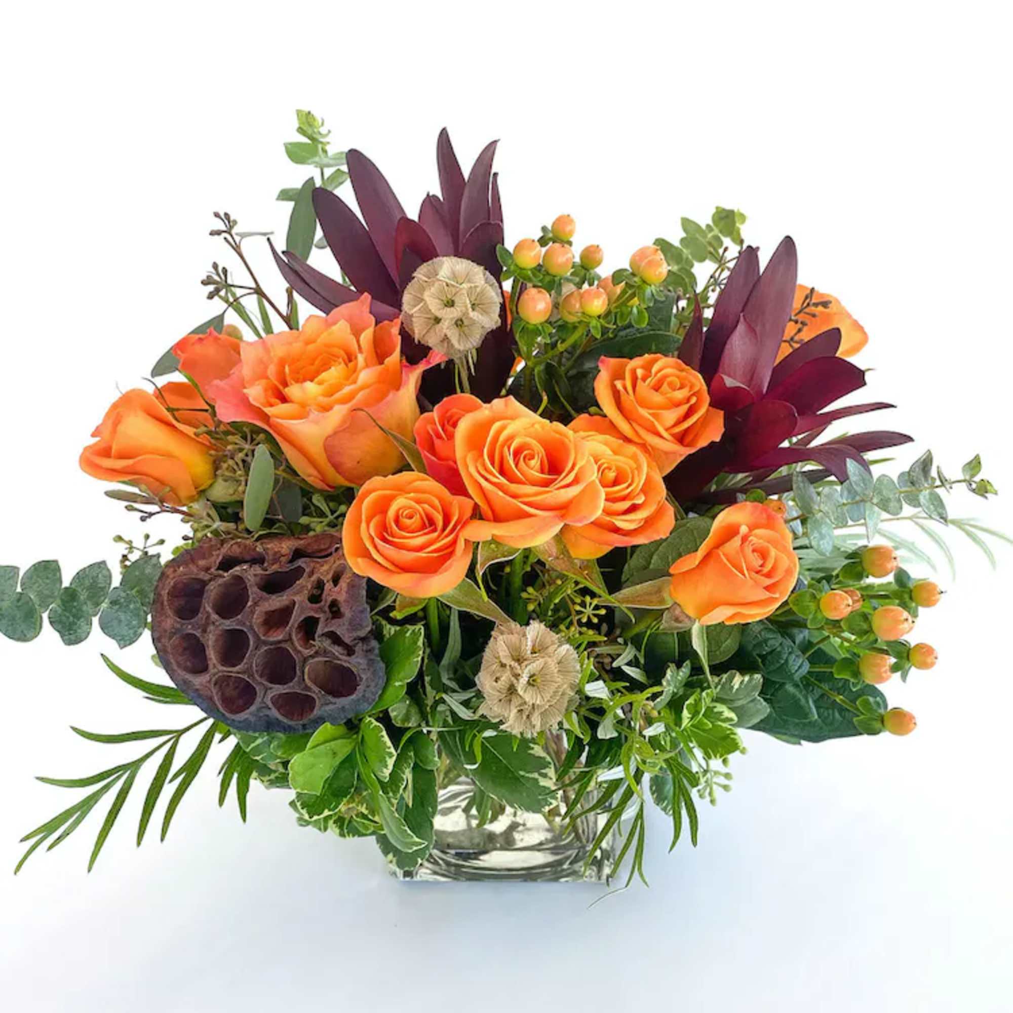 Orange roses in a glass vase with dark burgundy foliage and berries