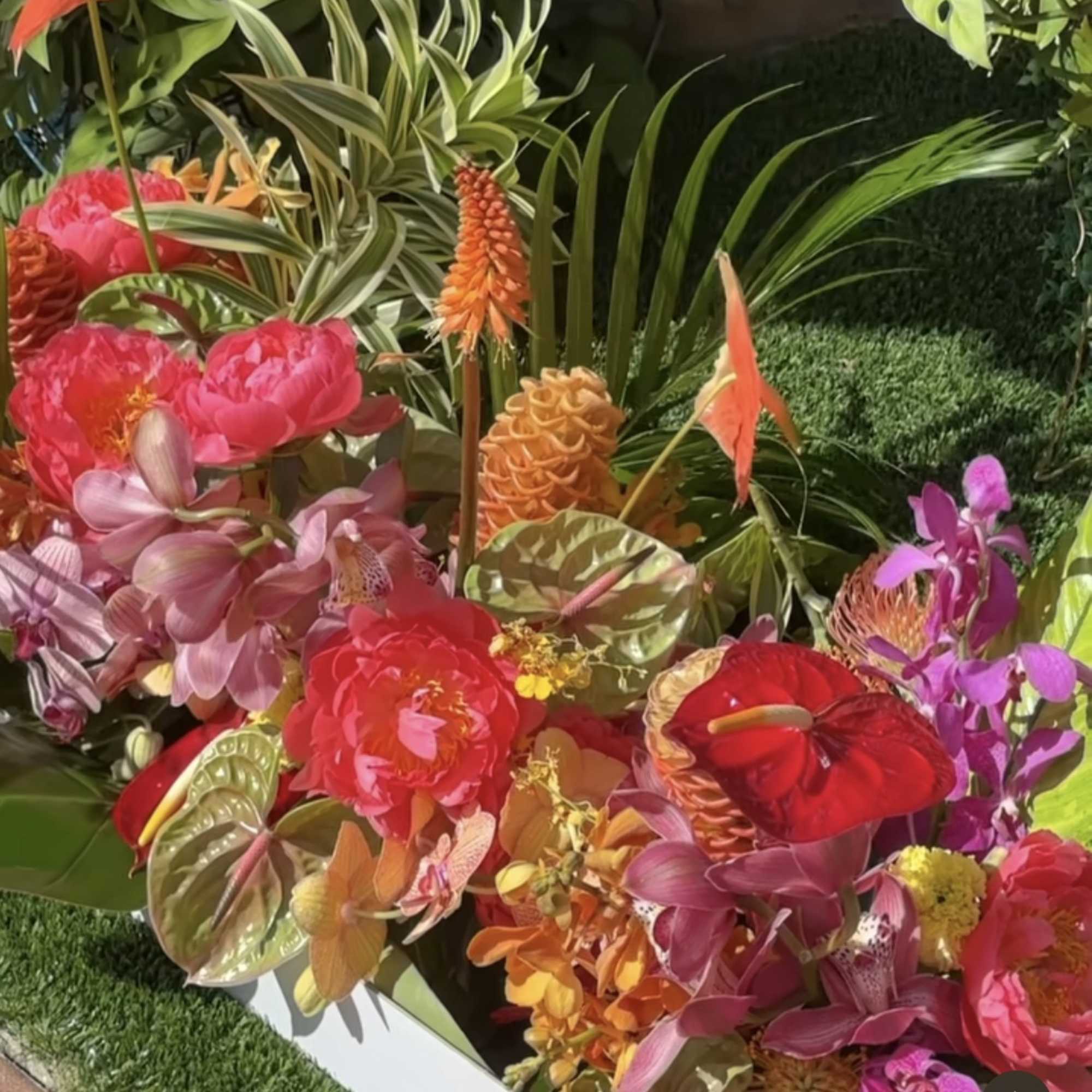 Tropical floral arrangement with pink and orange blooms in a white container
