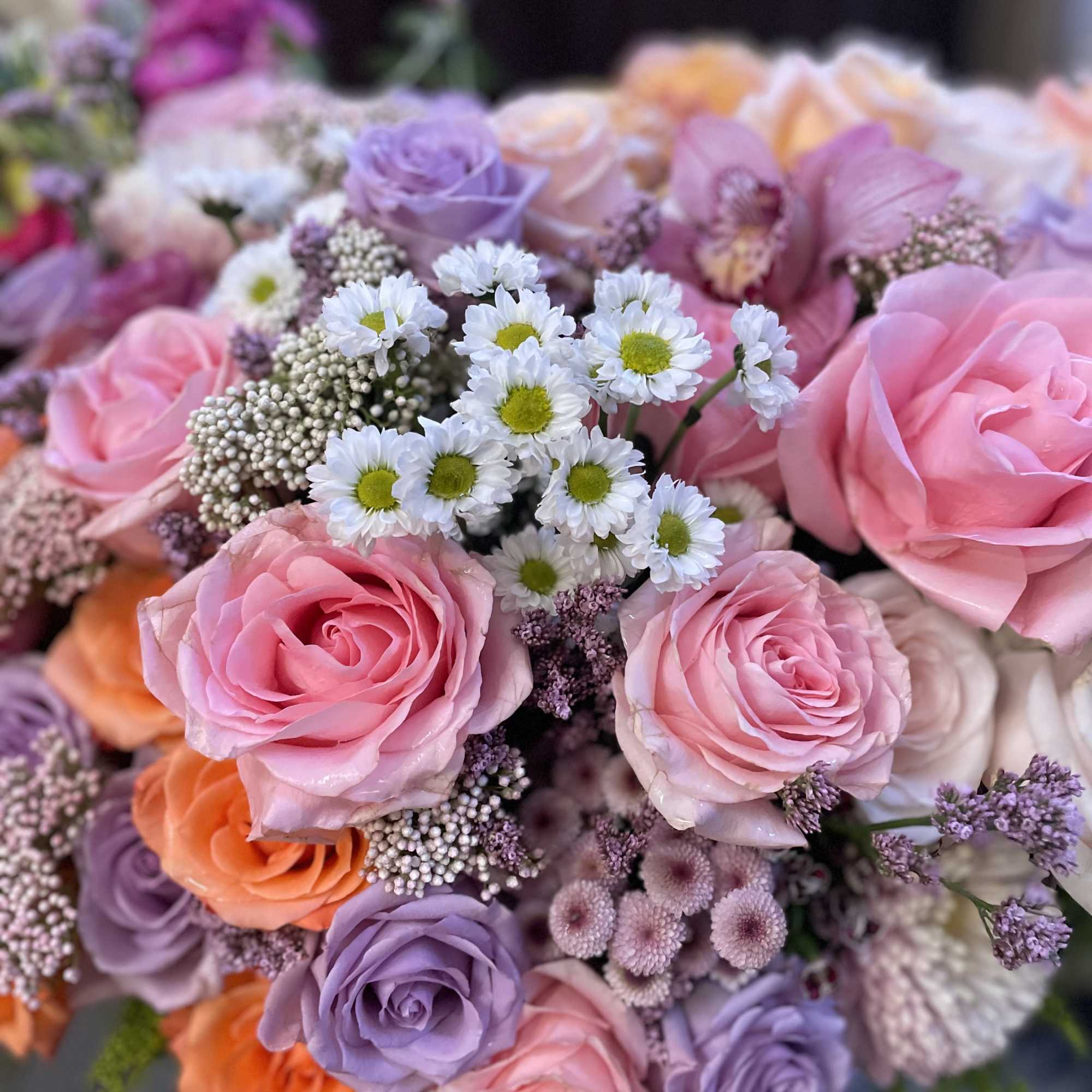 Bouquet of pink, lavender, and peach roses with small white daisies