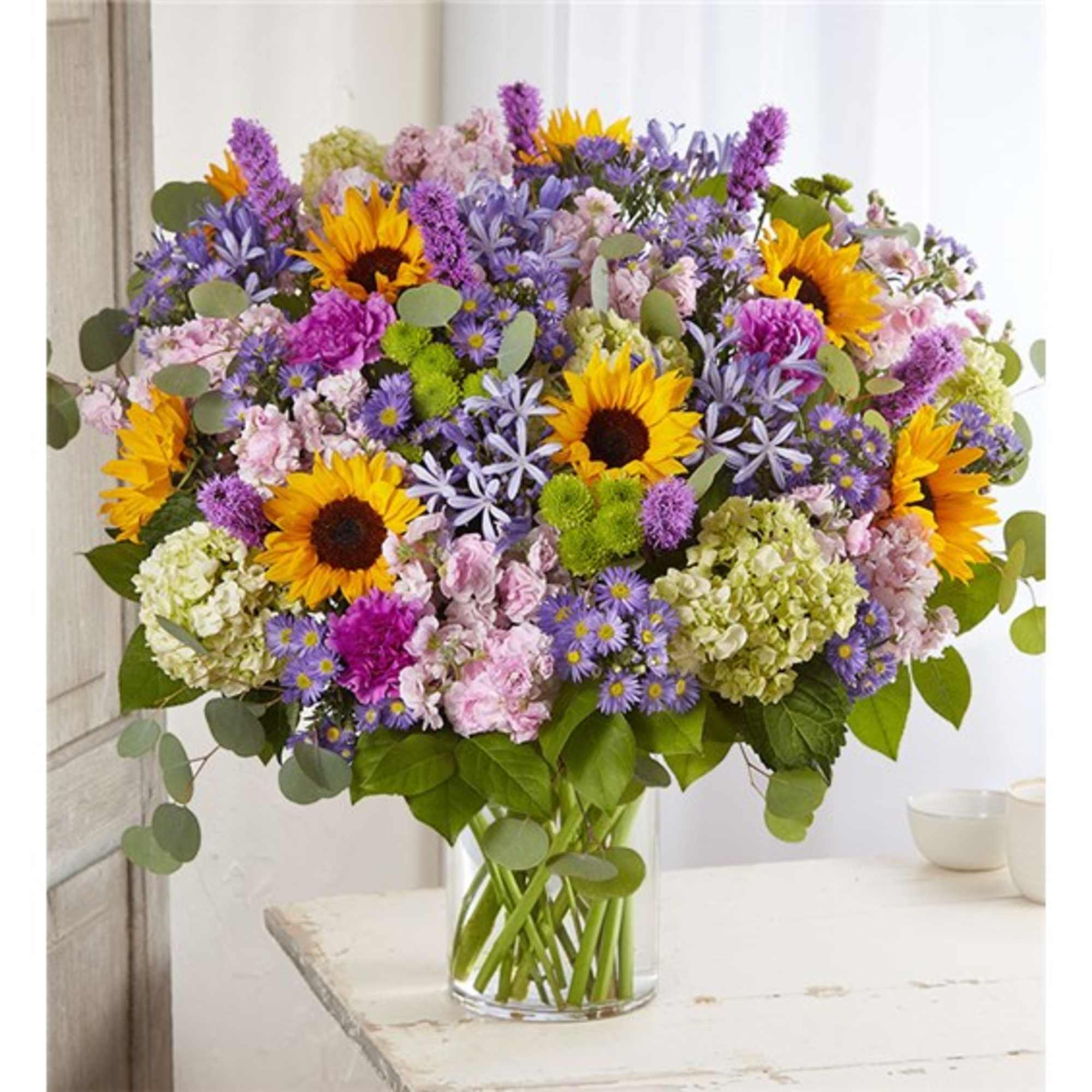 Mixed bouquet with sunflowers, purple blooms, and pink flowers in a glass vase