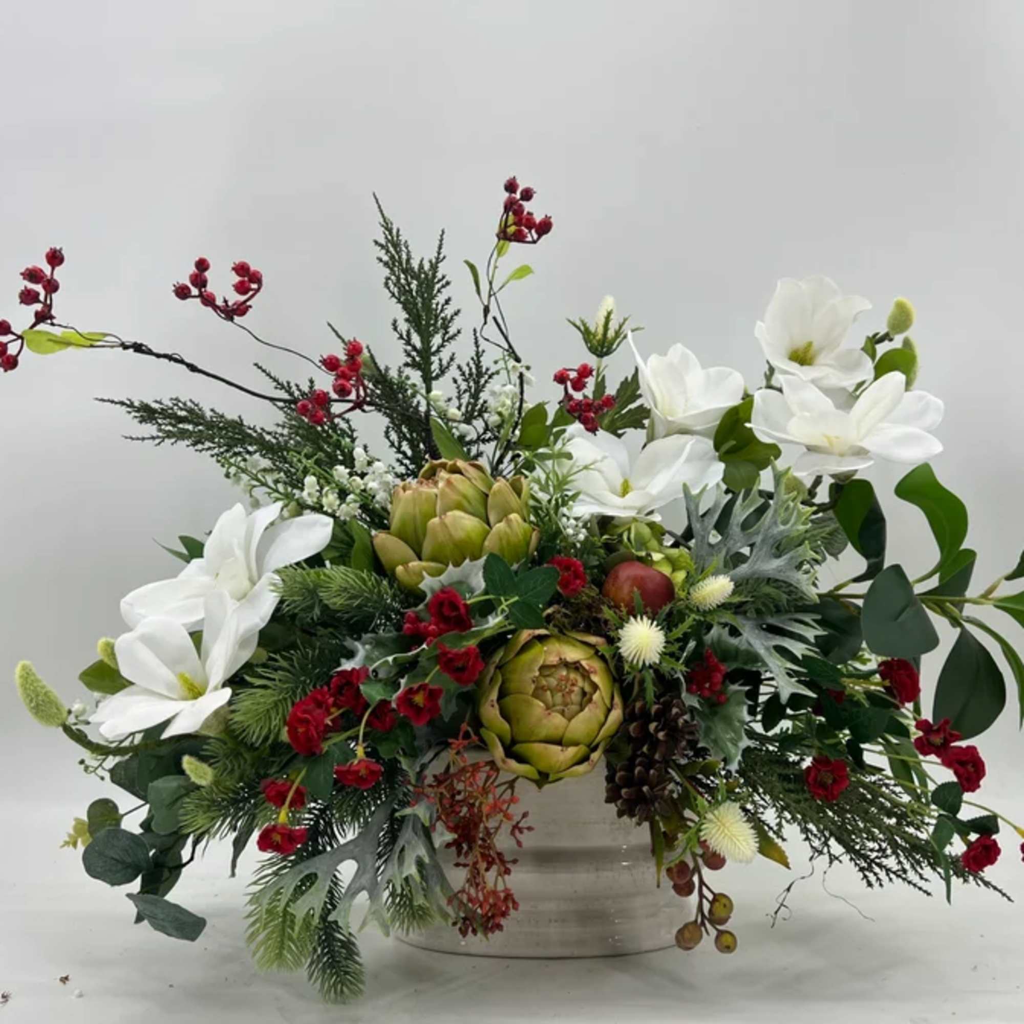 White flowers and red berries arranged in a low container with artichokes