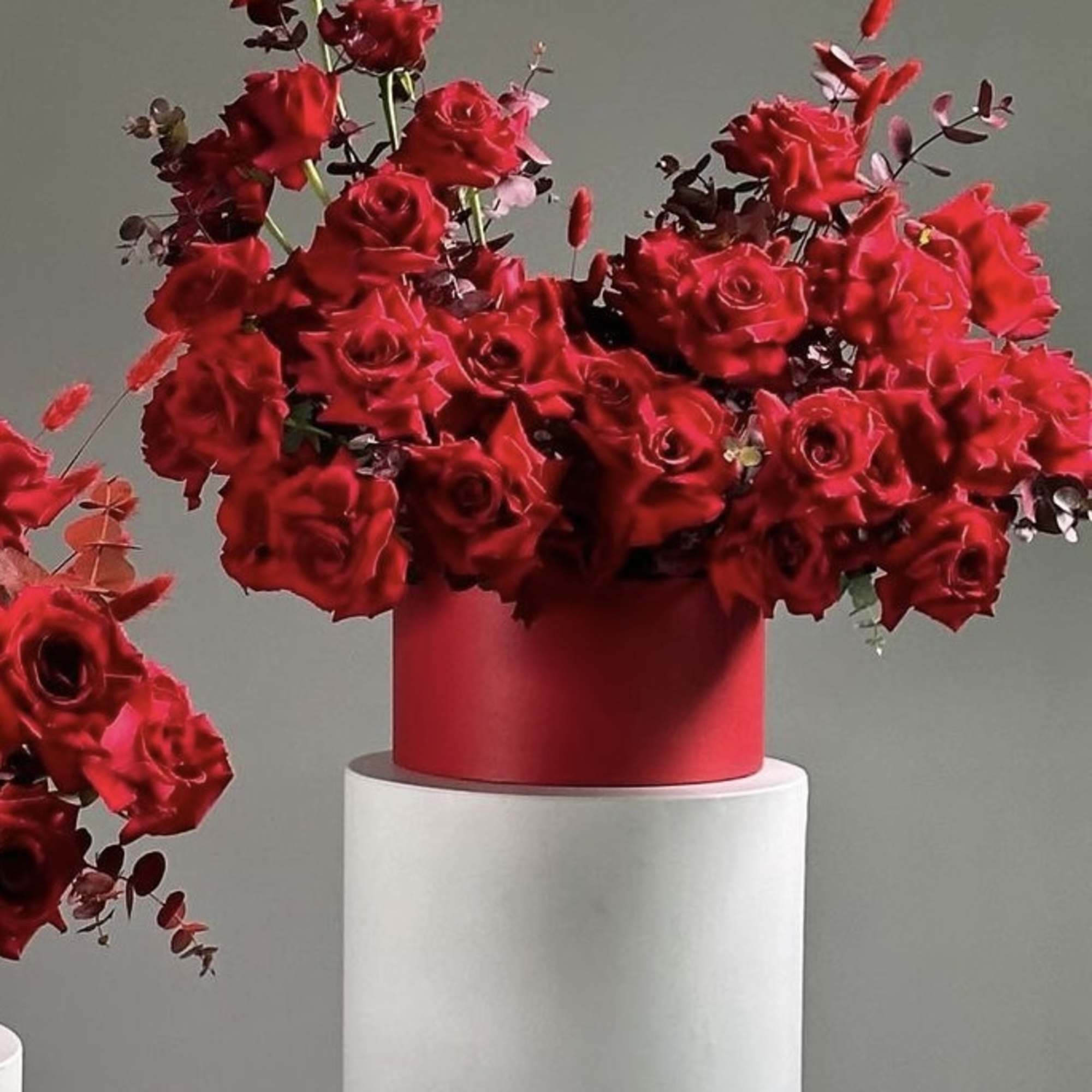 Red rose arrangement in a red cylindrical vase on a white pedestal