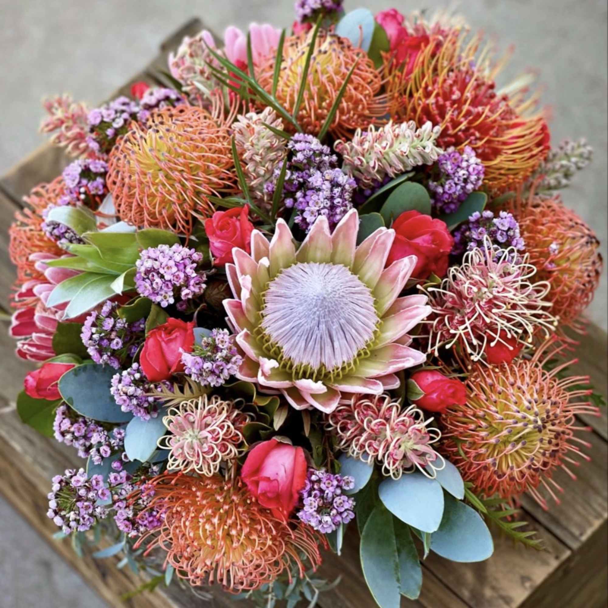 Colorful bouquet with pink protea, red roses, and purple filler flowers