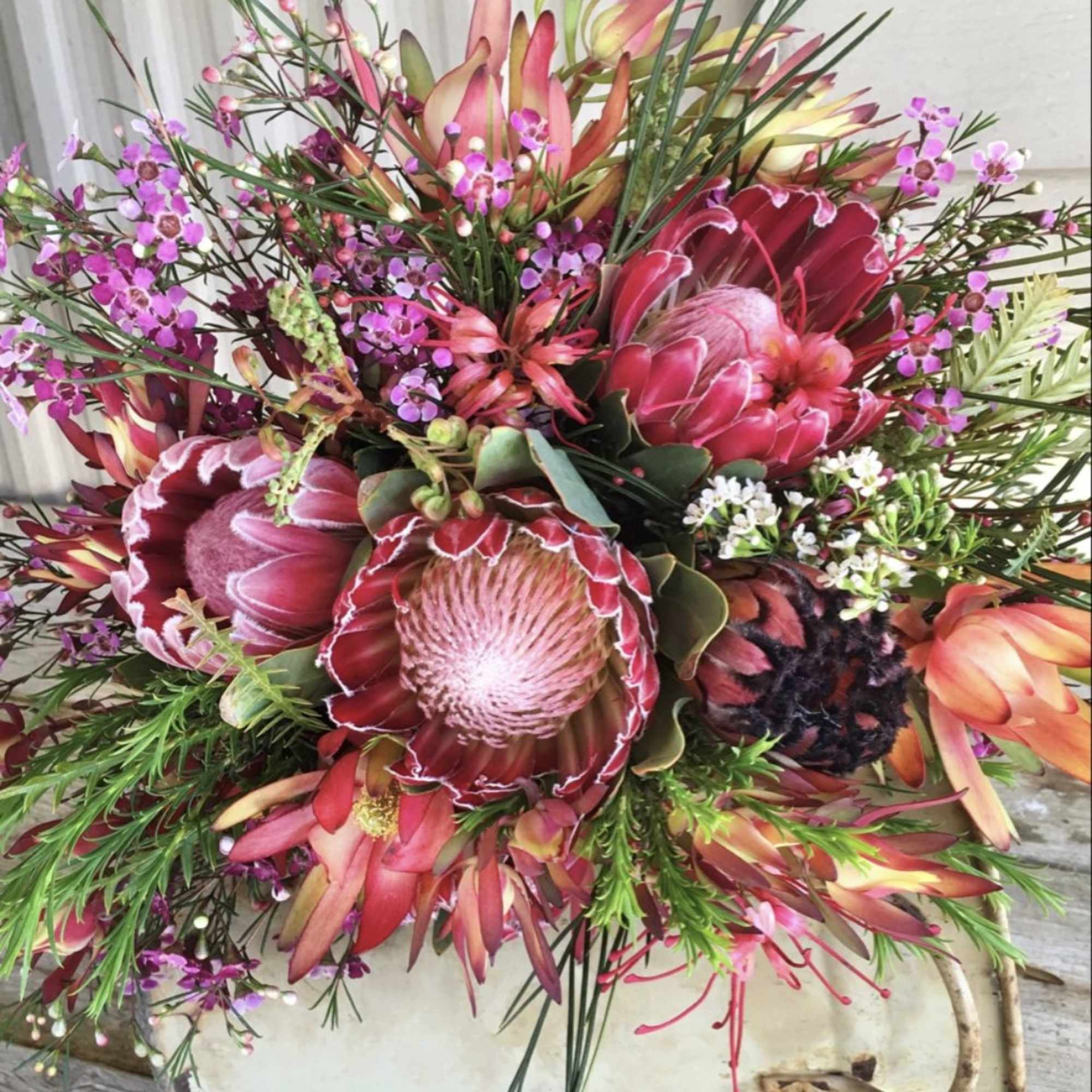 Mixed bouquet with pink protea and small purple flowers in a white container