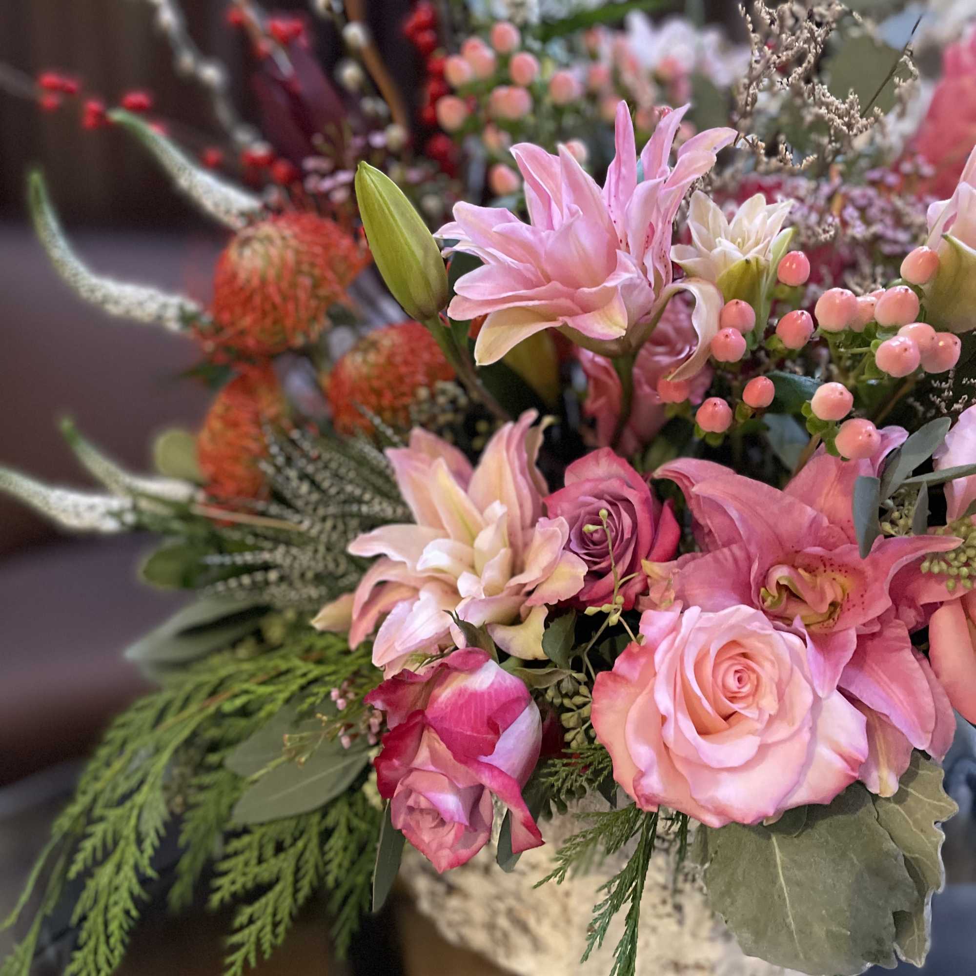 Pink roses and lilies arranged in a basket with berries and greenery