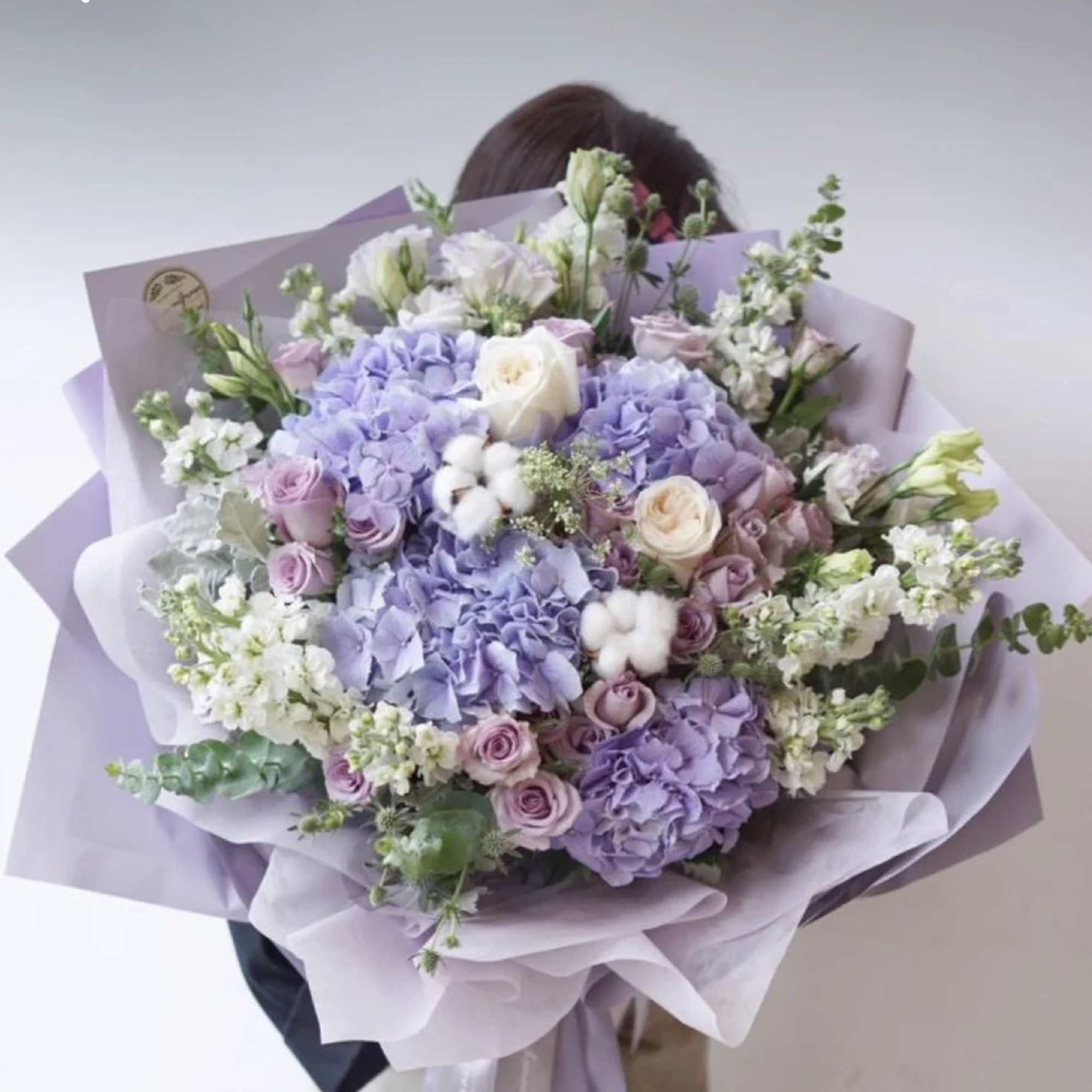 Large bouquet of lavender hydrangeas and pale roses wrapped in lilac paper