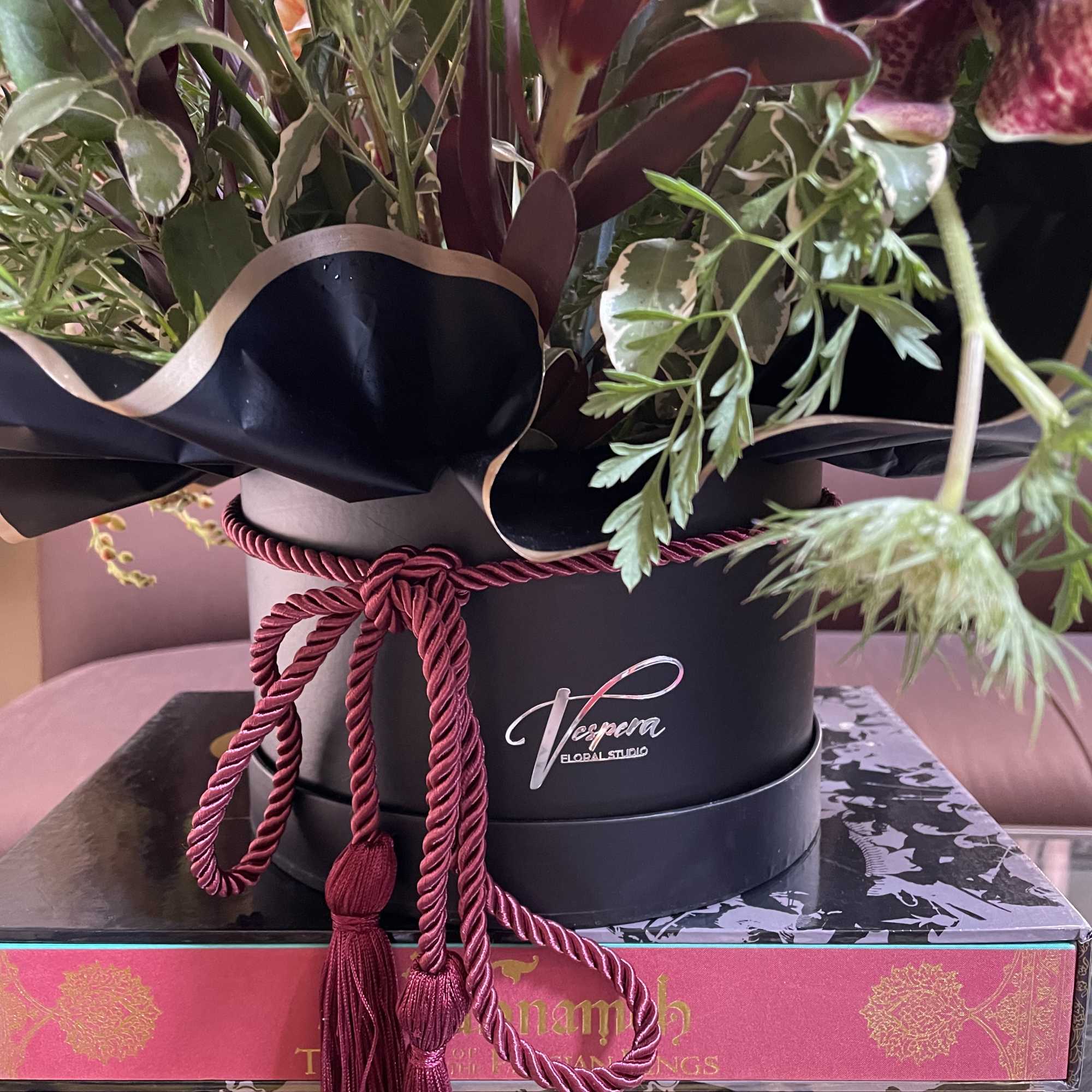 Mixed floral arrangement in a black hatbox with a burgundy cord tassel