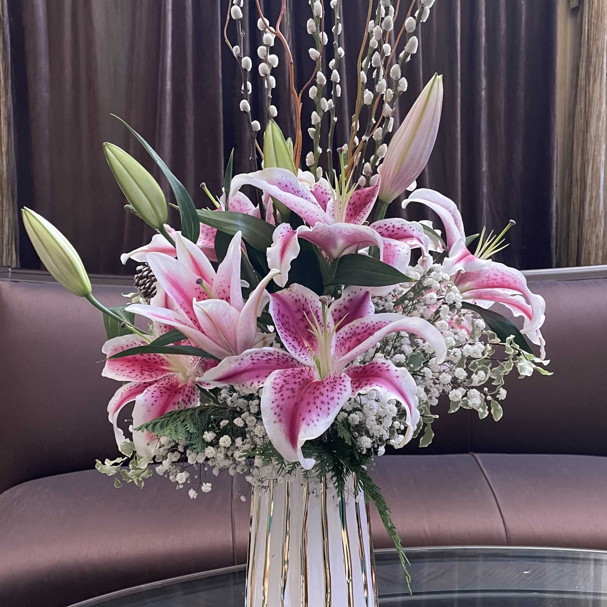 Pink stargazer lilies arranged in a tall white vase with gold stripes
