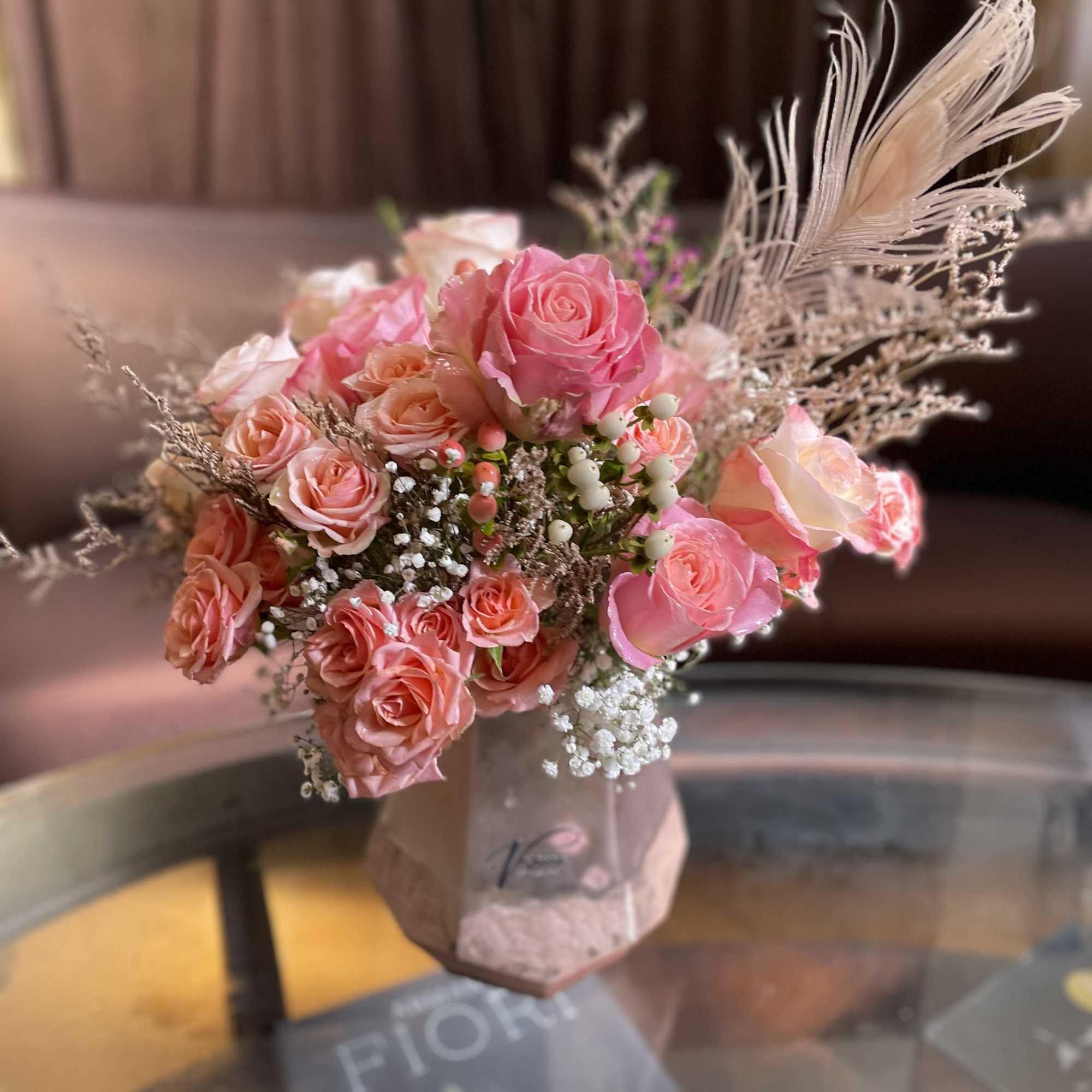 Pink rose bouquet in a vase with white filler and feather accents