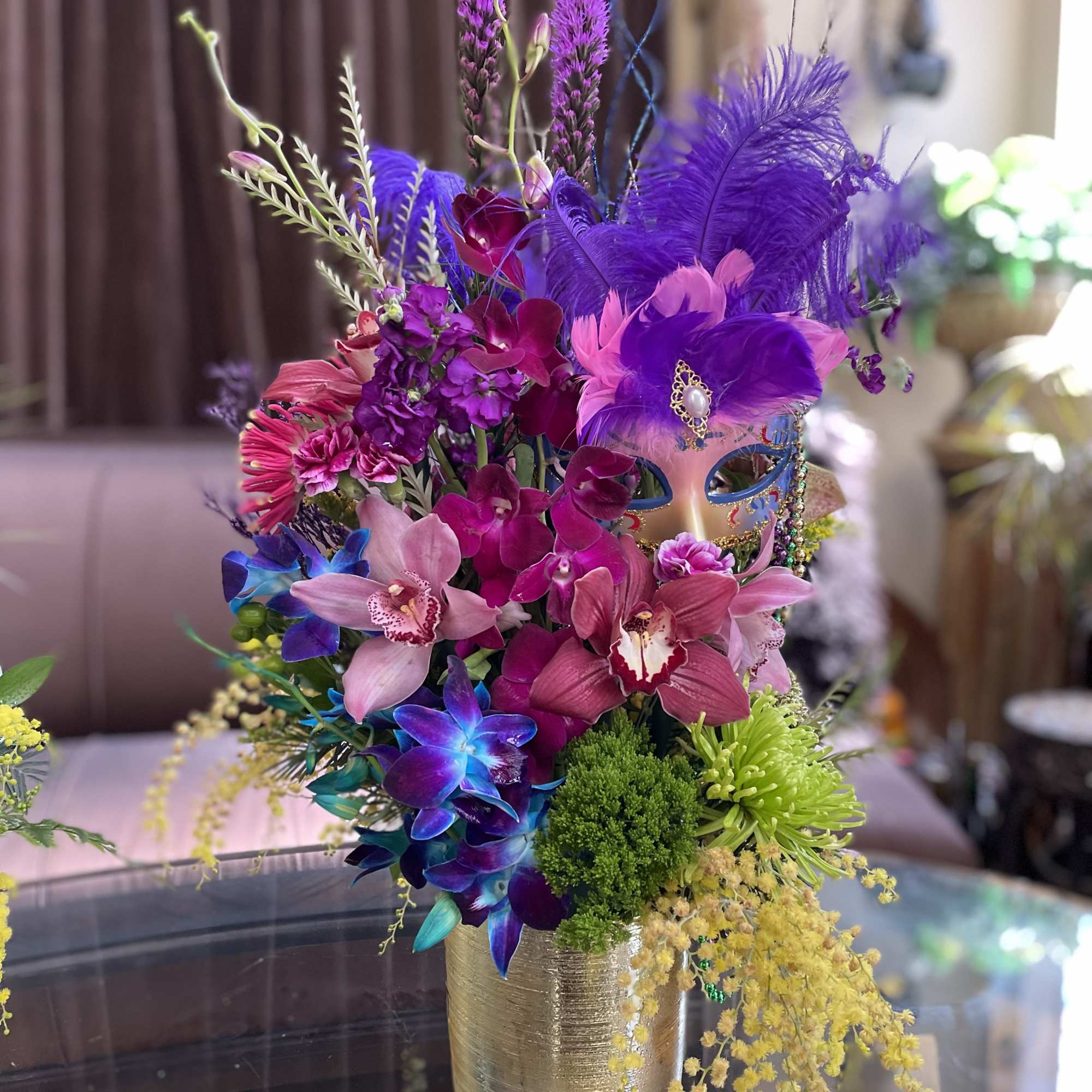 Colorful bouquet with orchids, feathers, and a decorative mask in a gold vase
