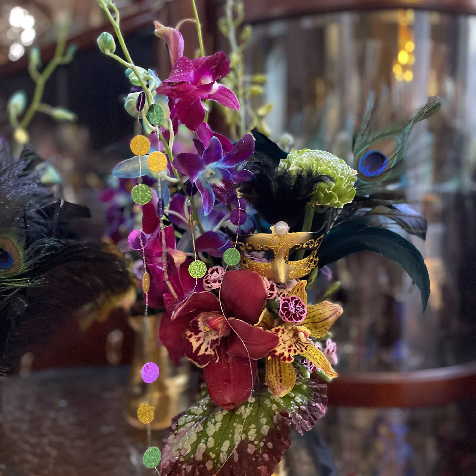 Tropical orchid arrangement with feathers and a gold mask in a vase