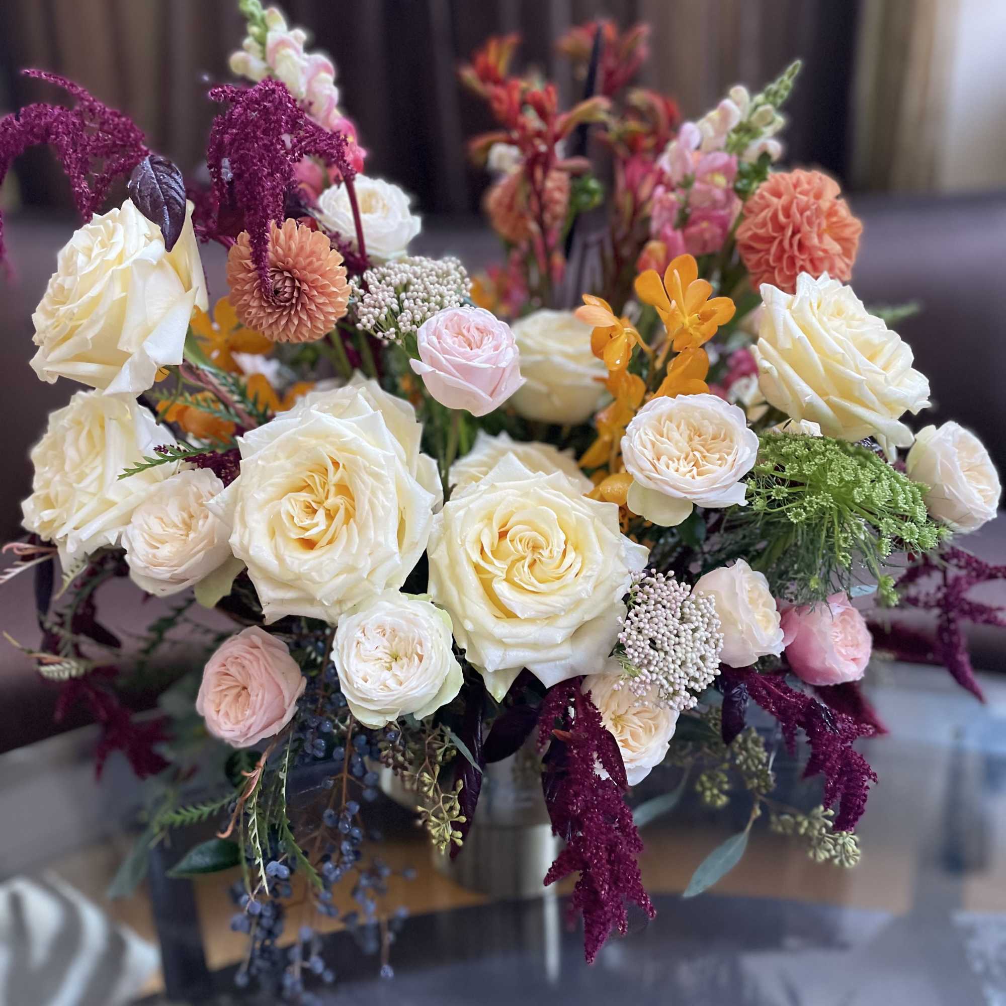 Mixed bouquet of cream roses, peach blooms, and magenta accents in a vase
