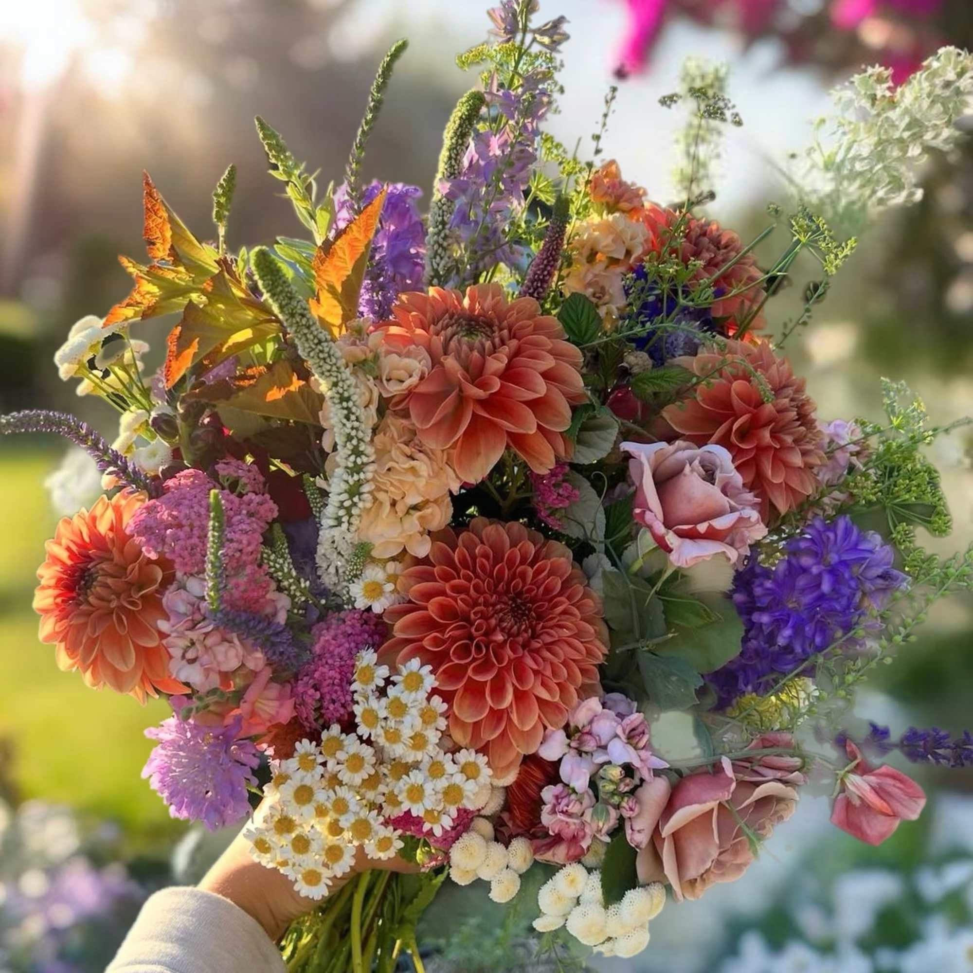 Handheld bouquet of orange, pink, purple, and white flowers