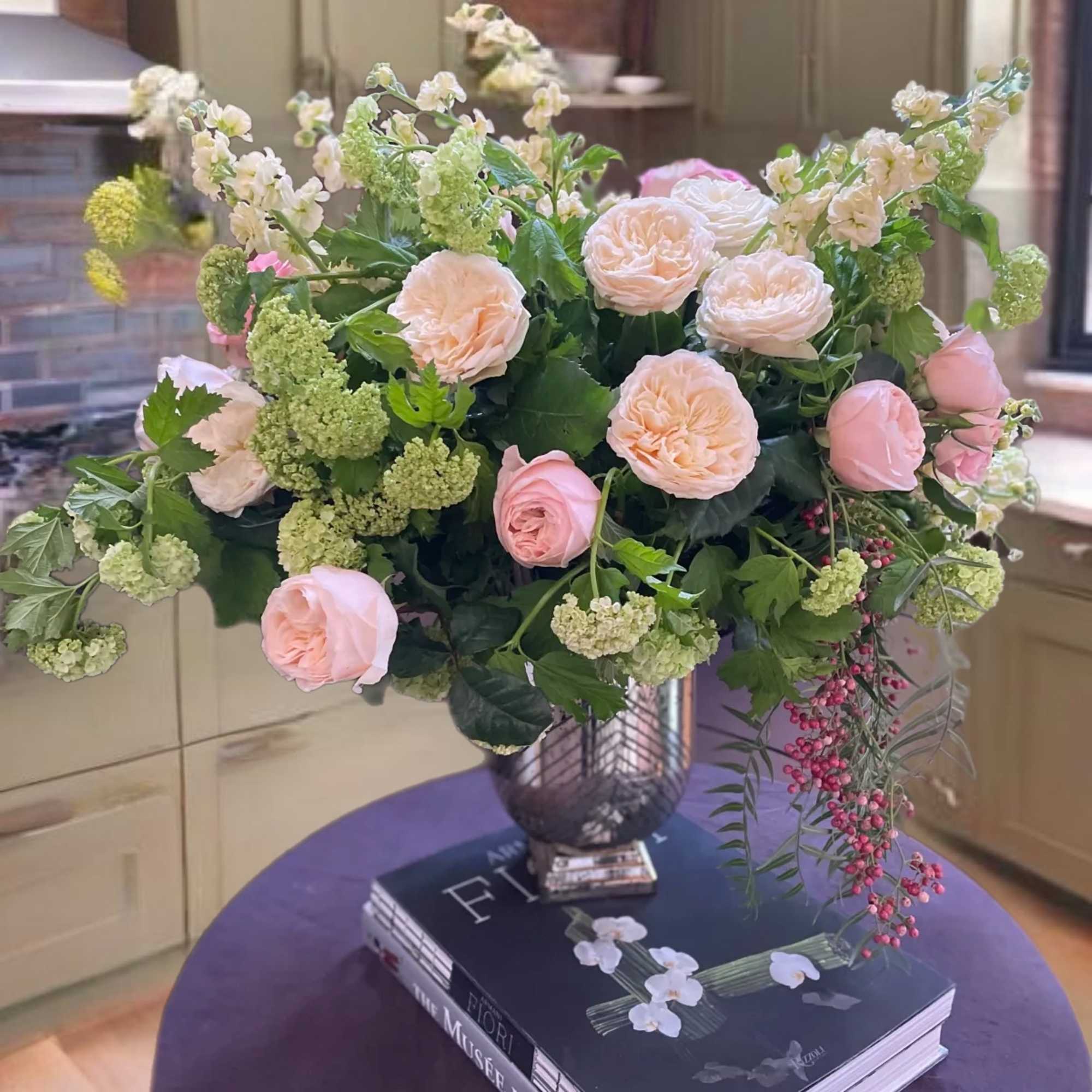 Blush roses and pale green blooms in a glass vase on a book stack