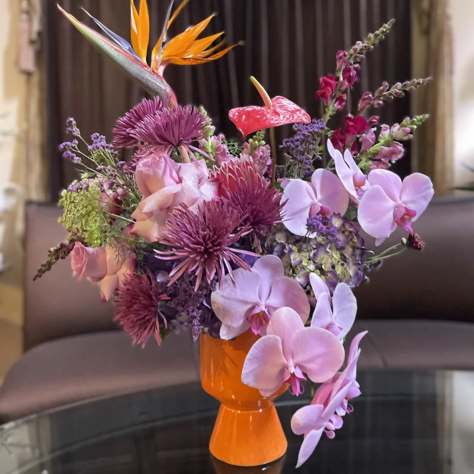 Mixed bouquet with orchids, anthurium, and orange bird of paradise in a bright vase
