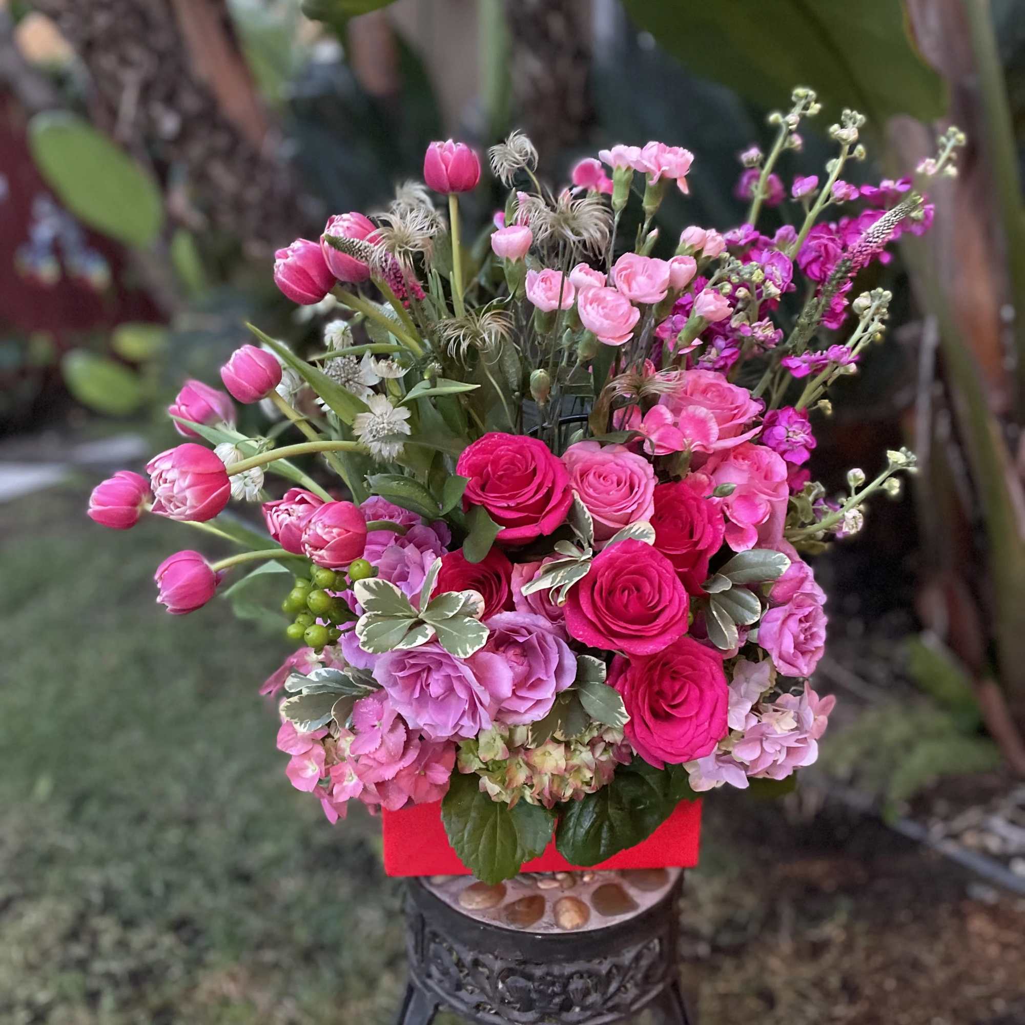 Pink and magenta flower arrangement in a red container