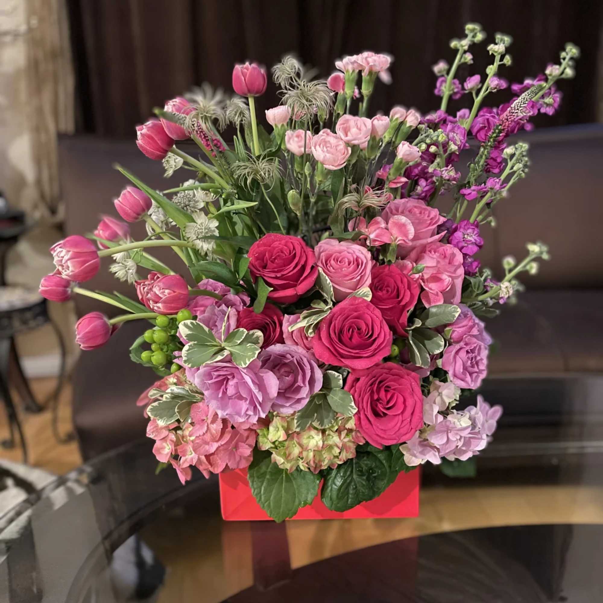 Pink and purple mixed flower arrangement in a red box
