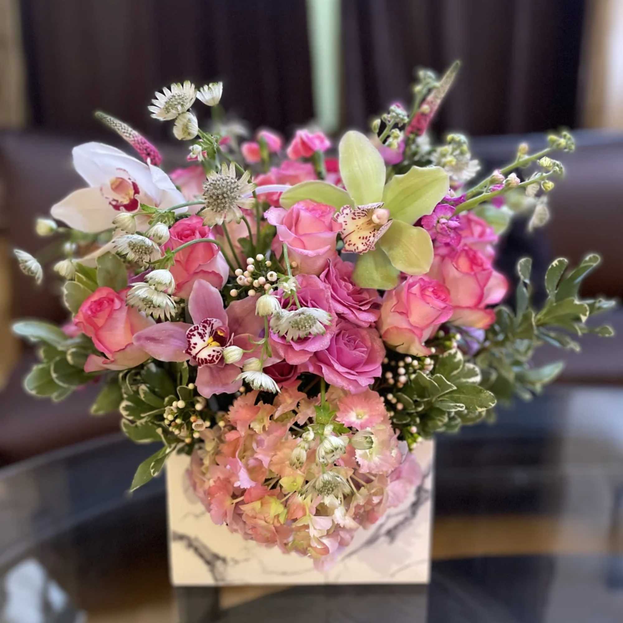 Pink rose and orchid arrangement in a white square vase