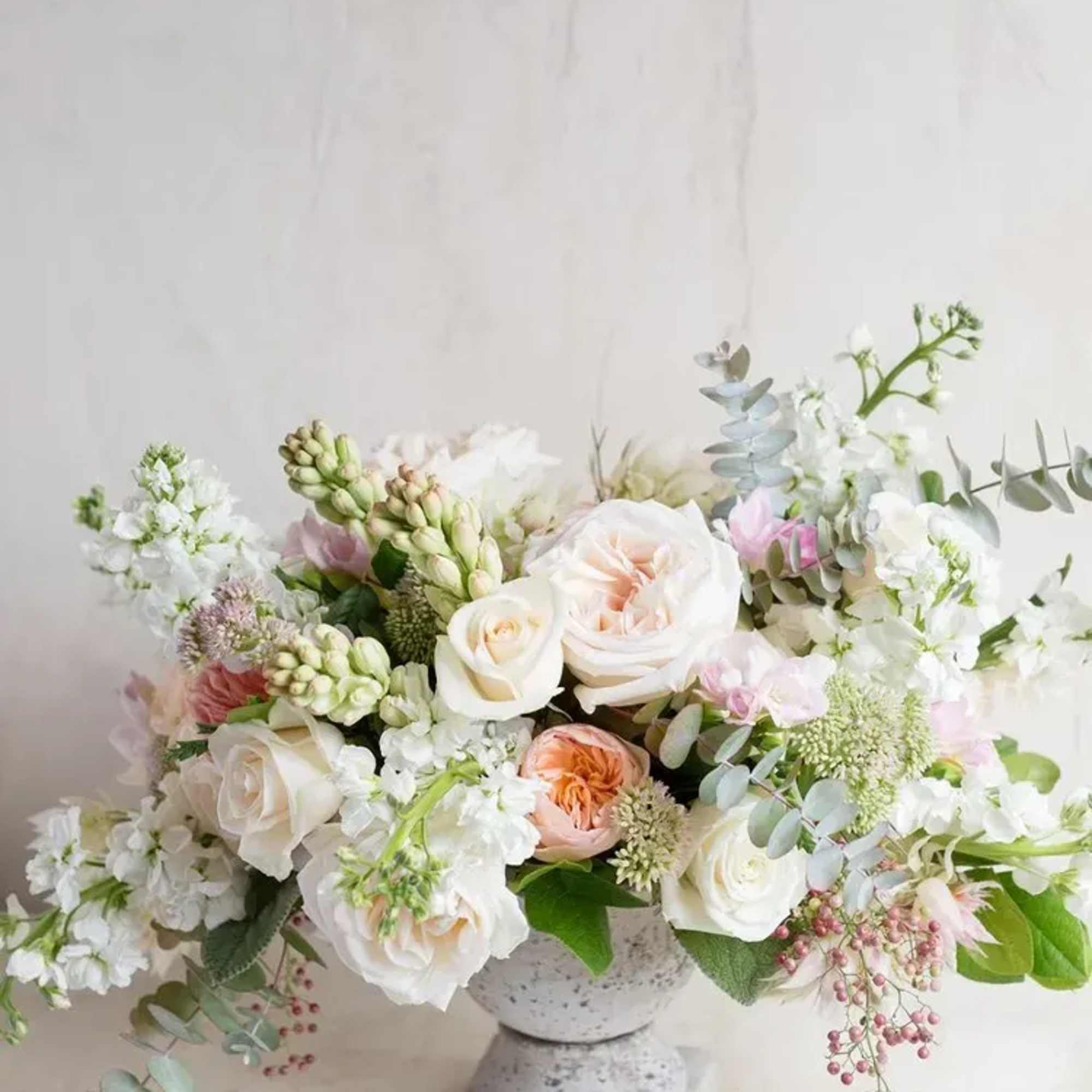 Soft pastel floral arrangement in a stone pedestal vase