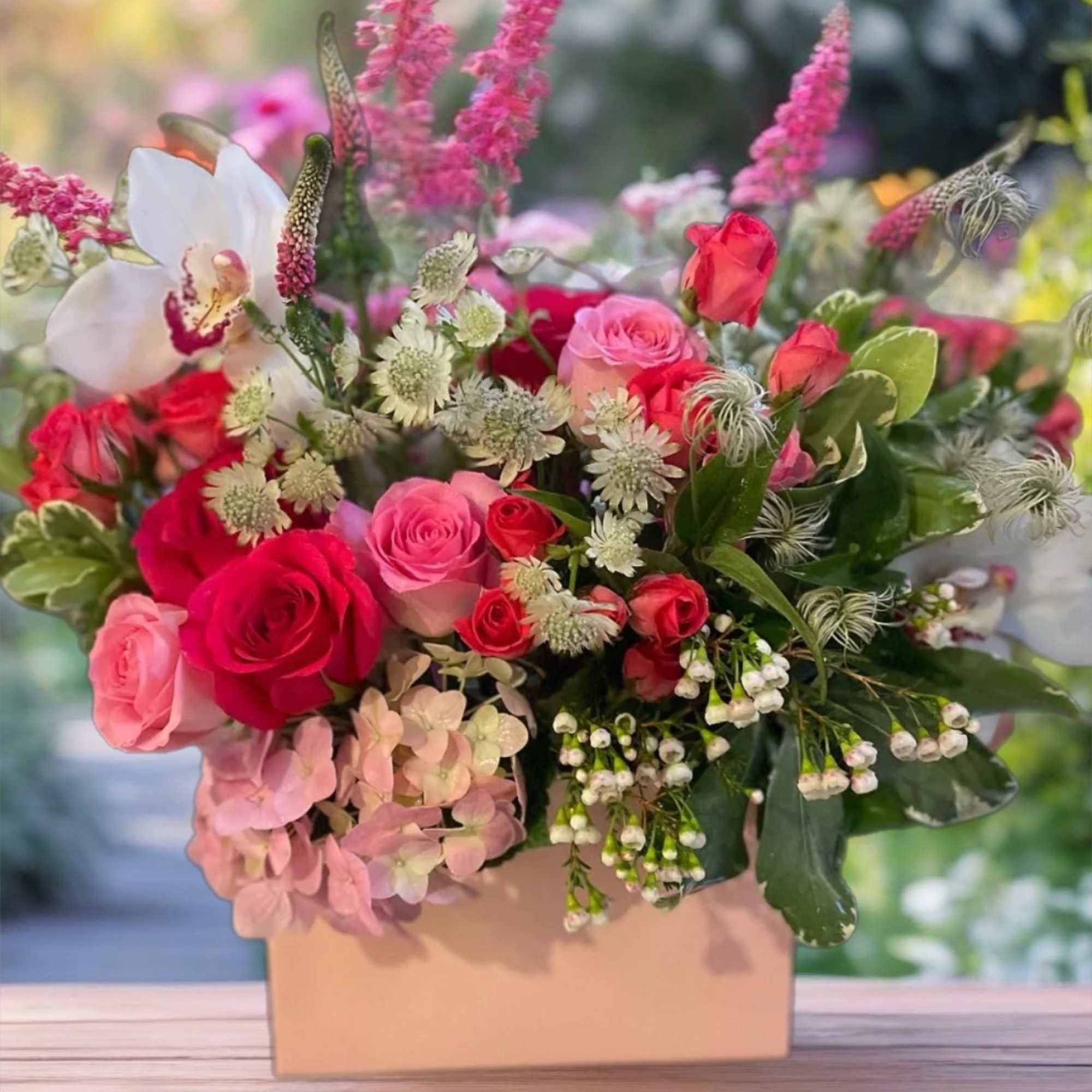 Pink and red roses with white orchids in a box arrangement