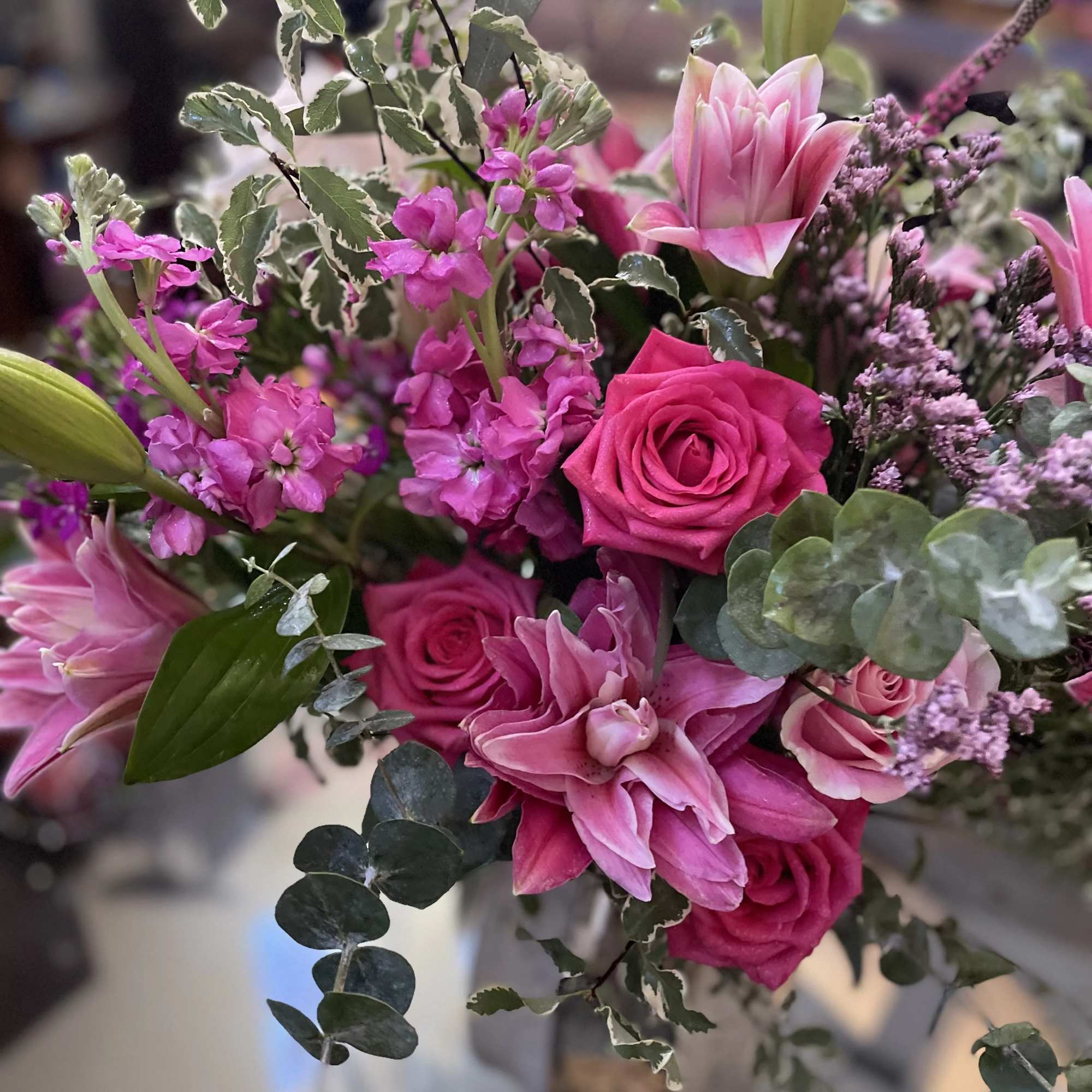 Pink roses and lilies arranged with purple filler flowers and variegated greenery