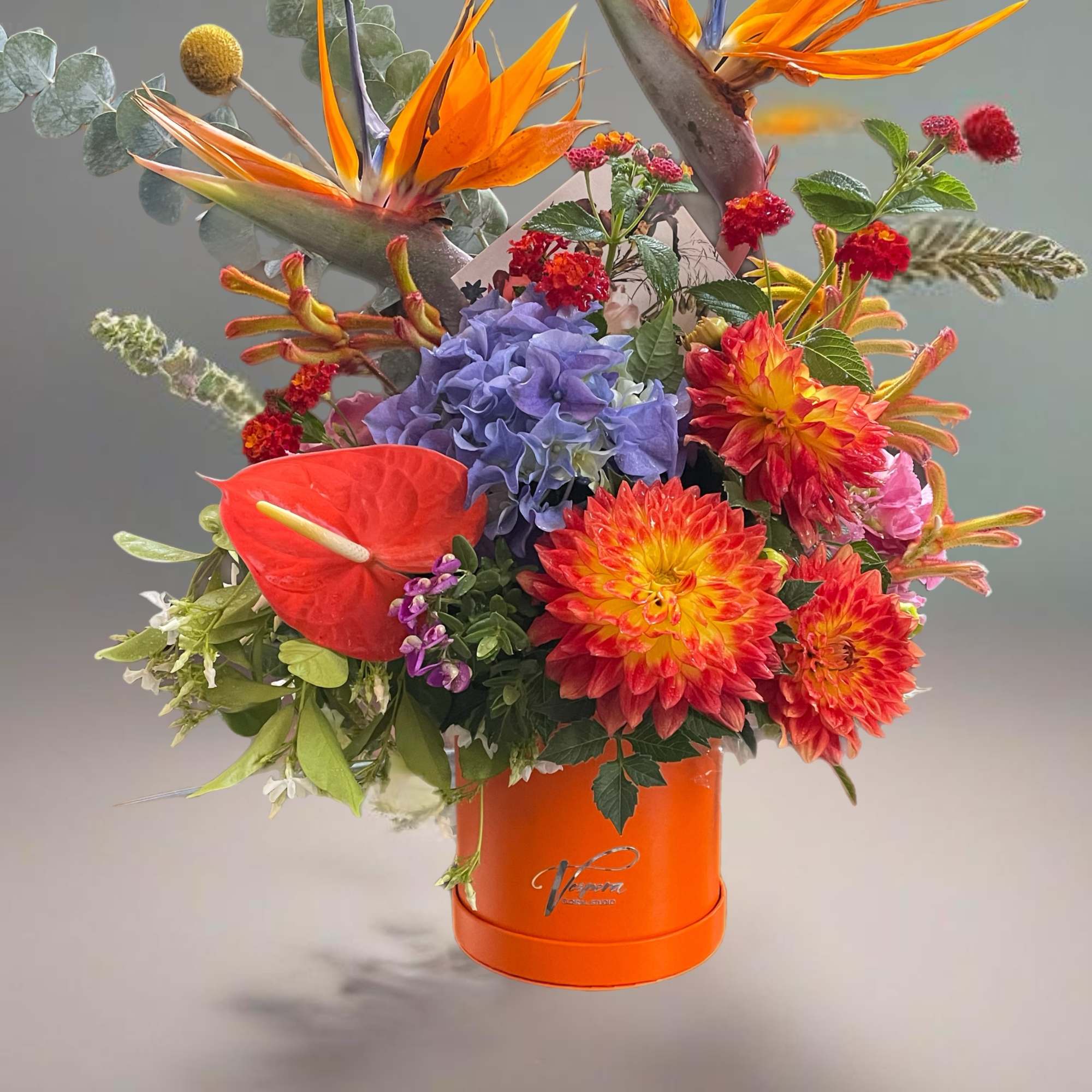 Tropical bouquet with orange bird-of-paradise and dahlias in an orange box