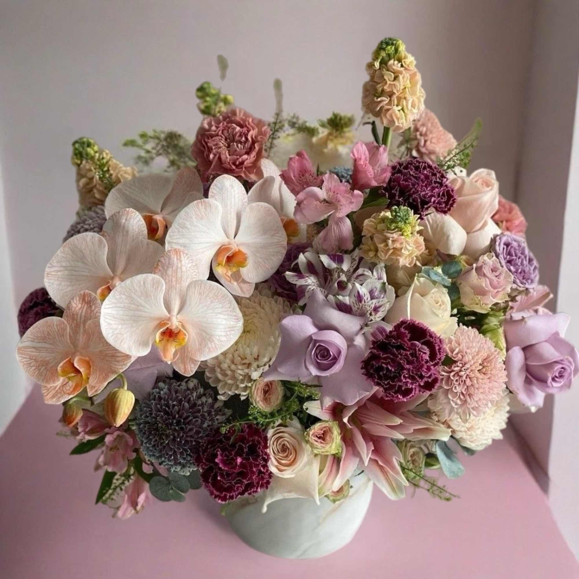 Pastel bouquet with orchids, roses, carnations, and chrysanthemums in a white vase