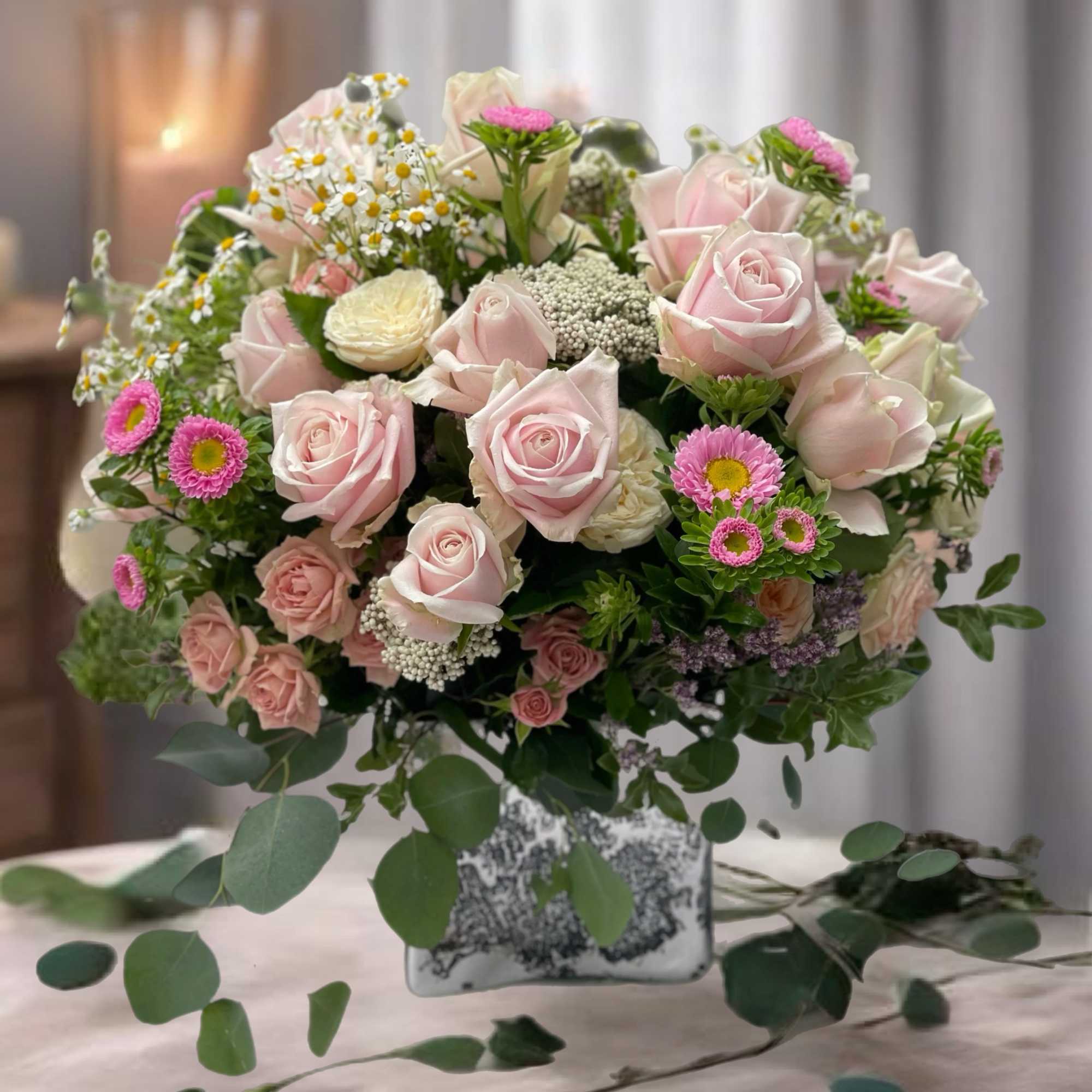 Pink roses and small daisies arranged in a square vase