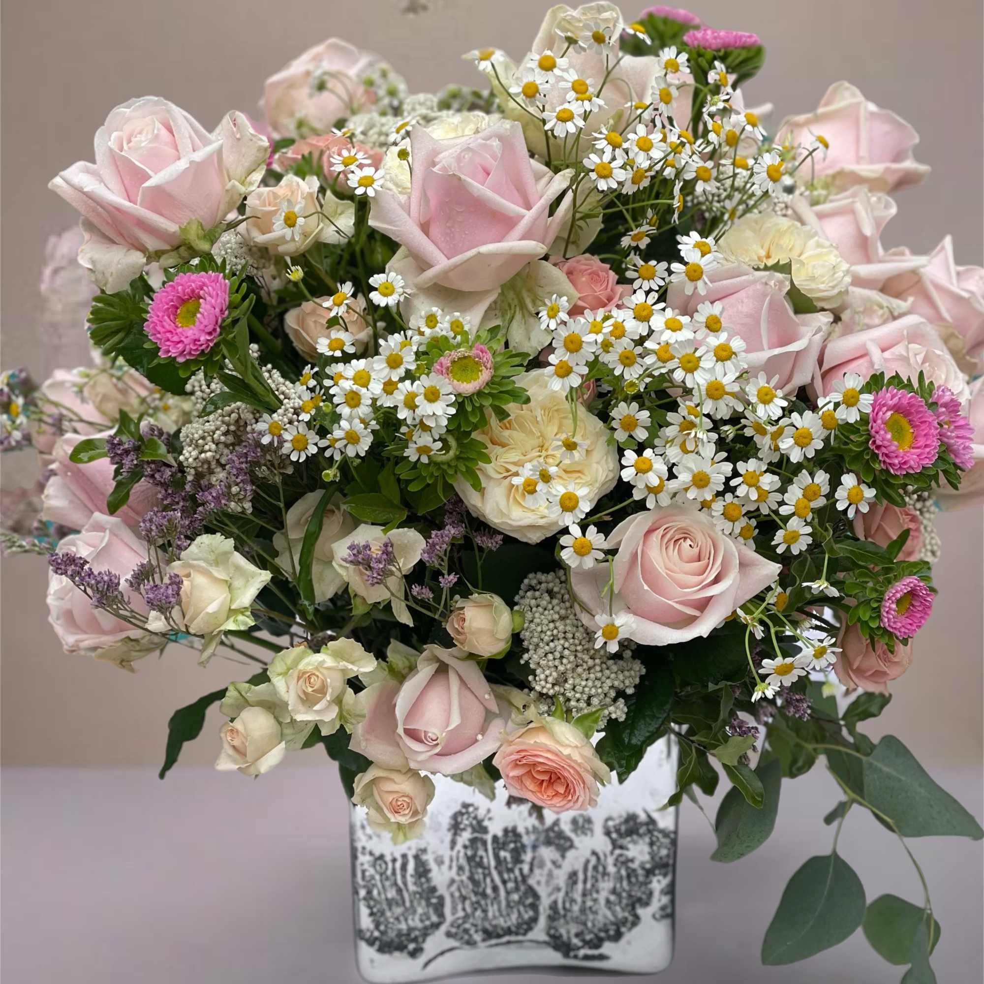 Pink roses and white daisies arranged in a square ceramic vase