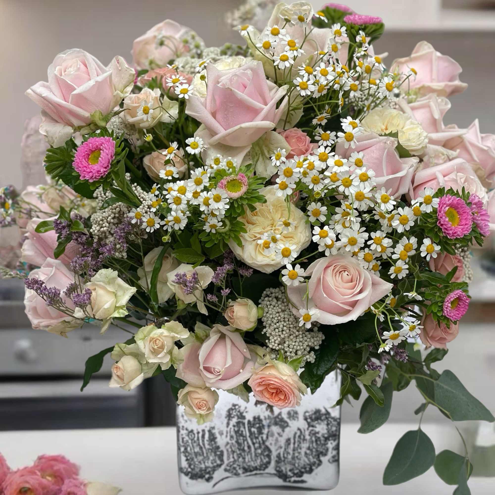 Pink roses and daisies arranged in a square vase