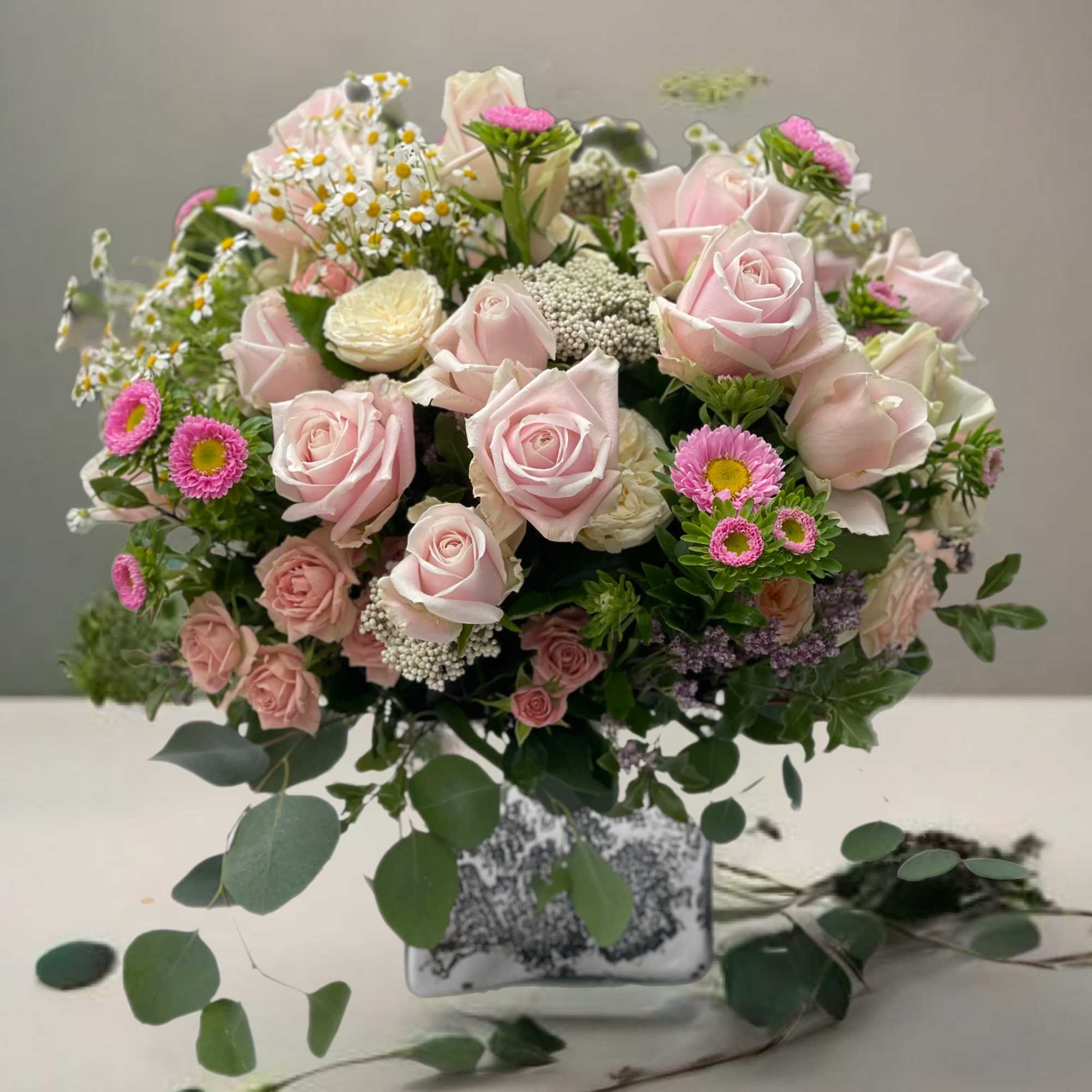 Pink rose bouquet in a square glass vase with small daisy-like blooms