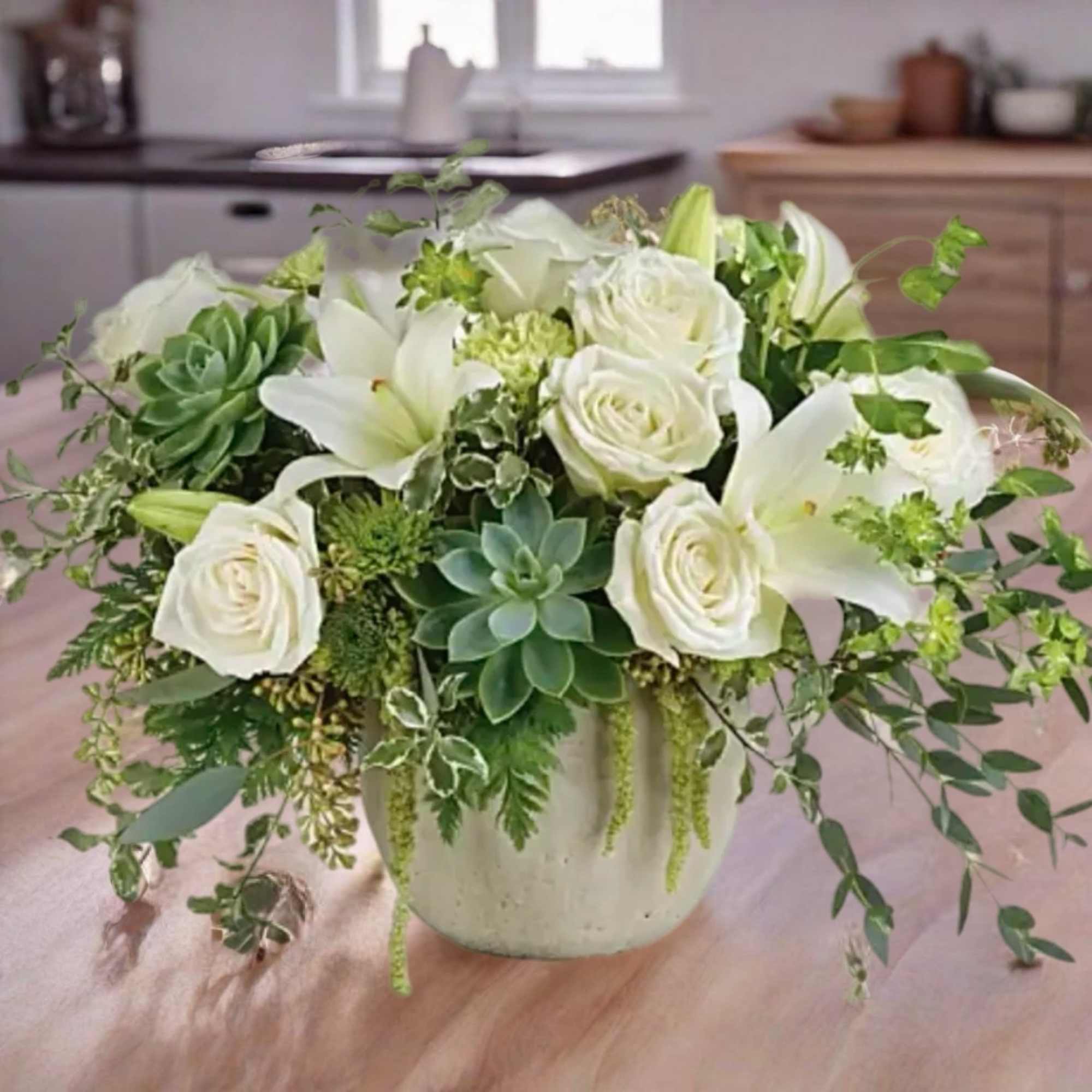 White roses and lilies arranged with succulents in a ceramic vase