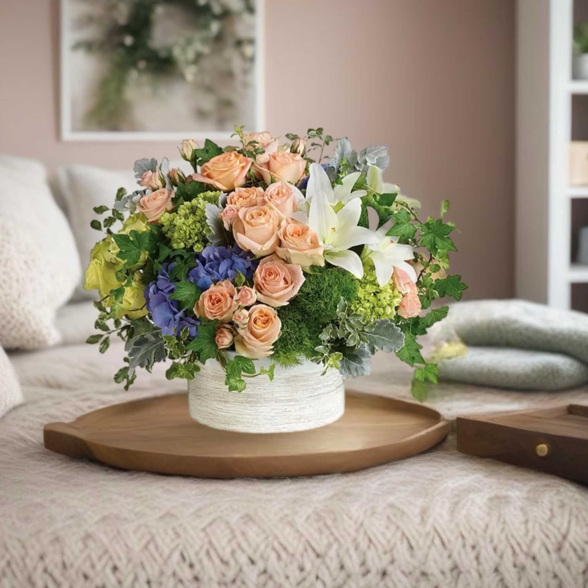 Mixed bouquet of peach roses, white lilies, and blue hydrangeas in a white vase