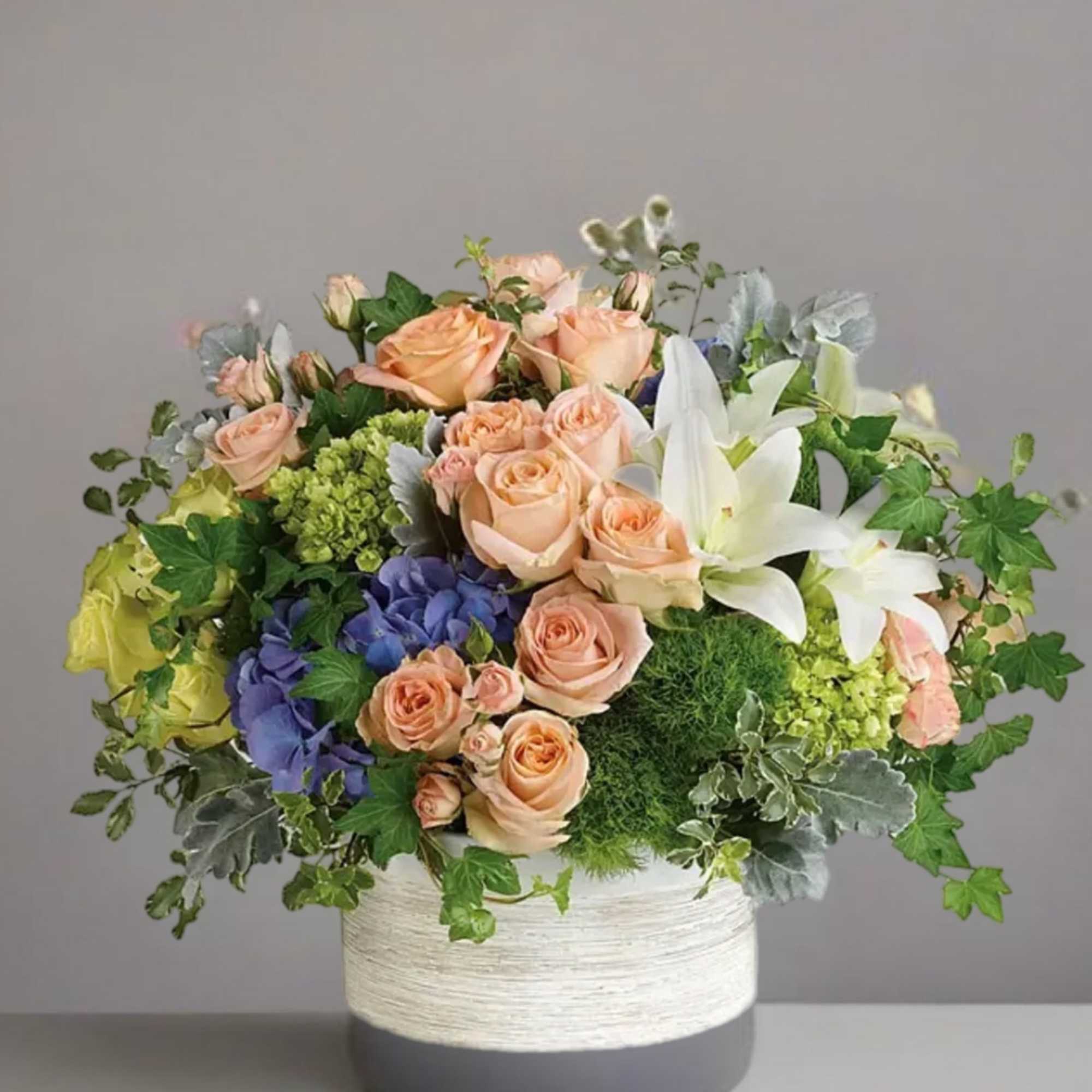 Peach roses and white lilies in a round white vase with greenery