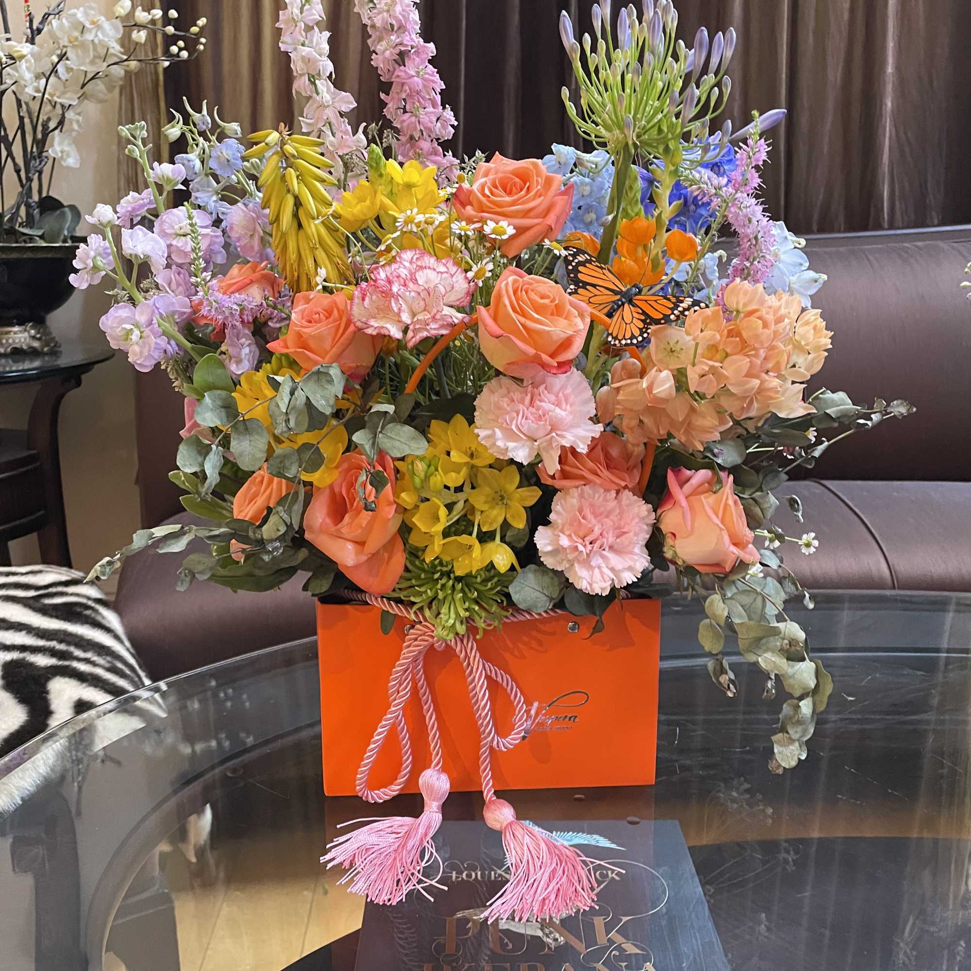 Colorful mixed flower arrangement in an orange gift box with pink tassels