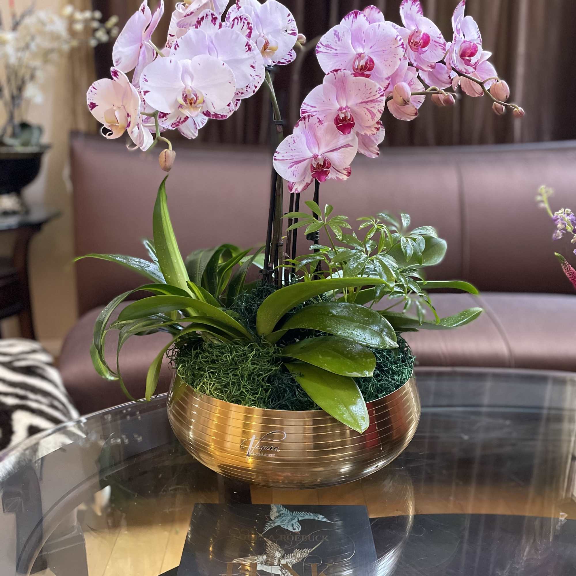 Pink orchid arrangement in a gold bowl on a glass table