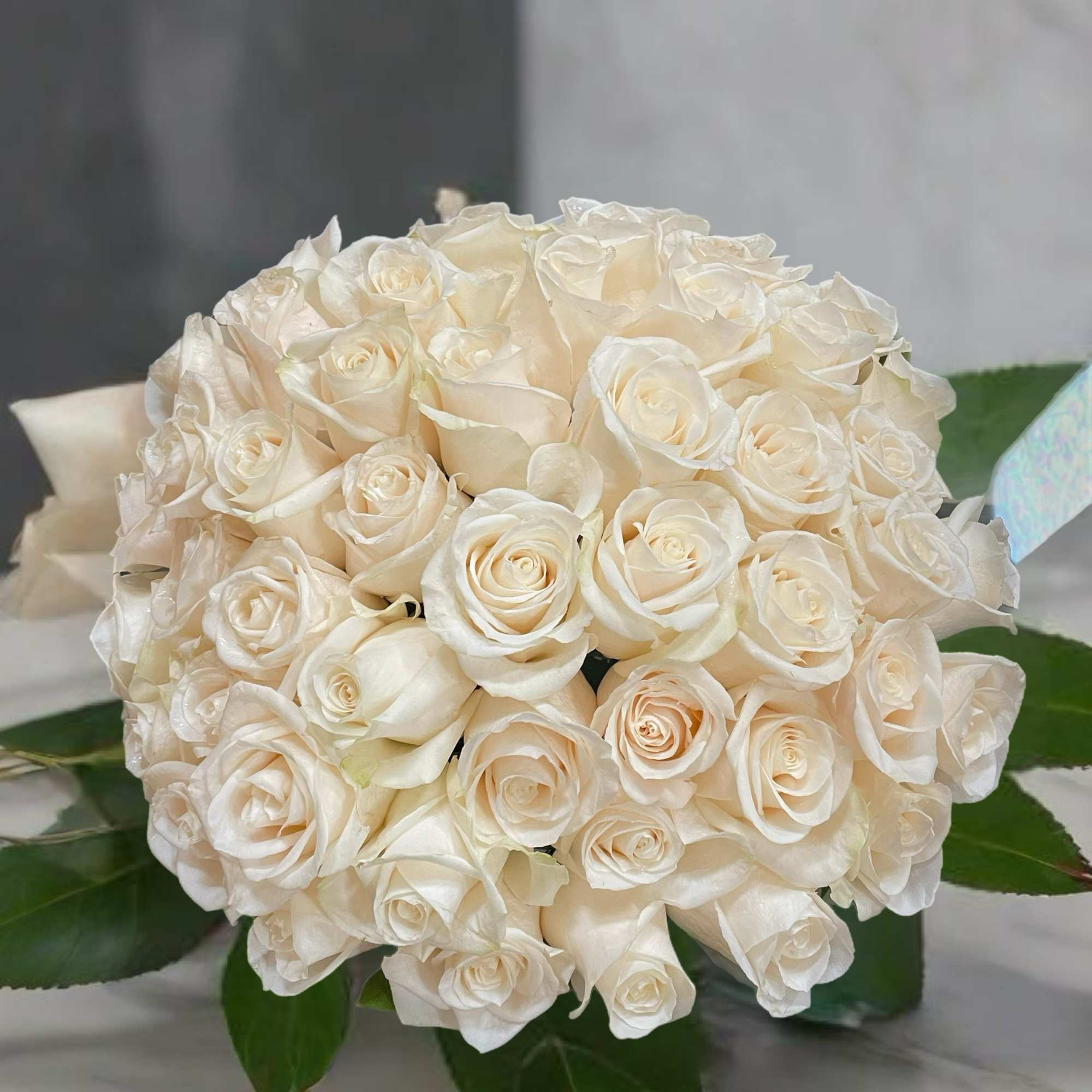 Round bouquet of white roses with dark green leaves