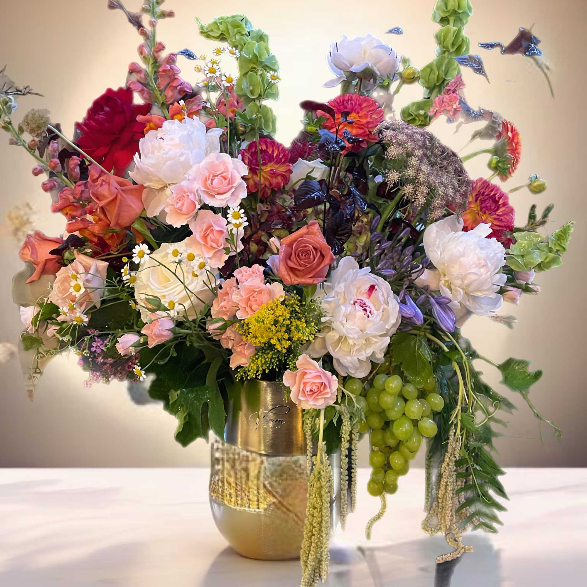 Large mixed floral arrangement in a gold vase with pink, white, and green blooms