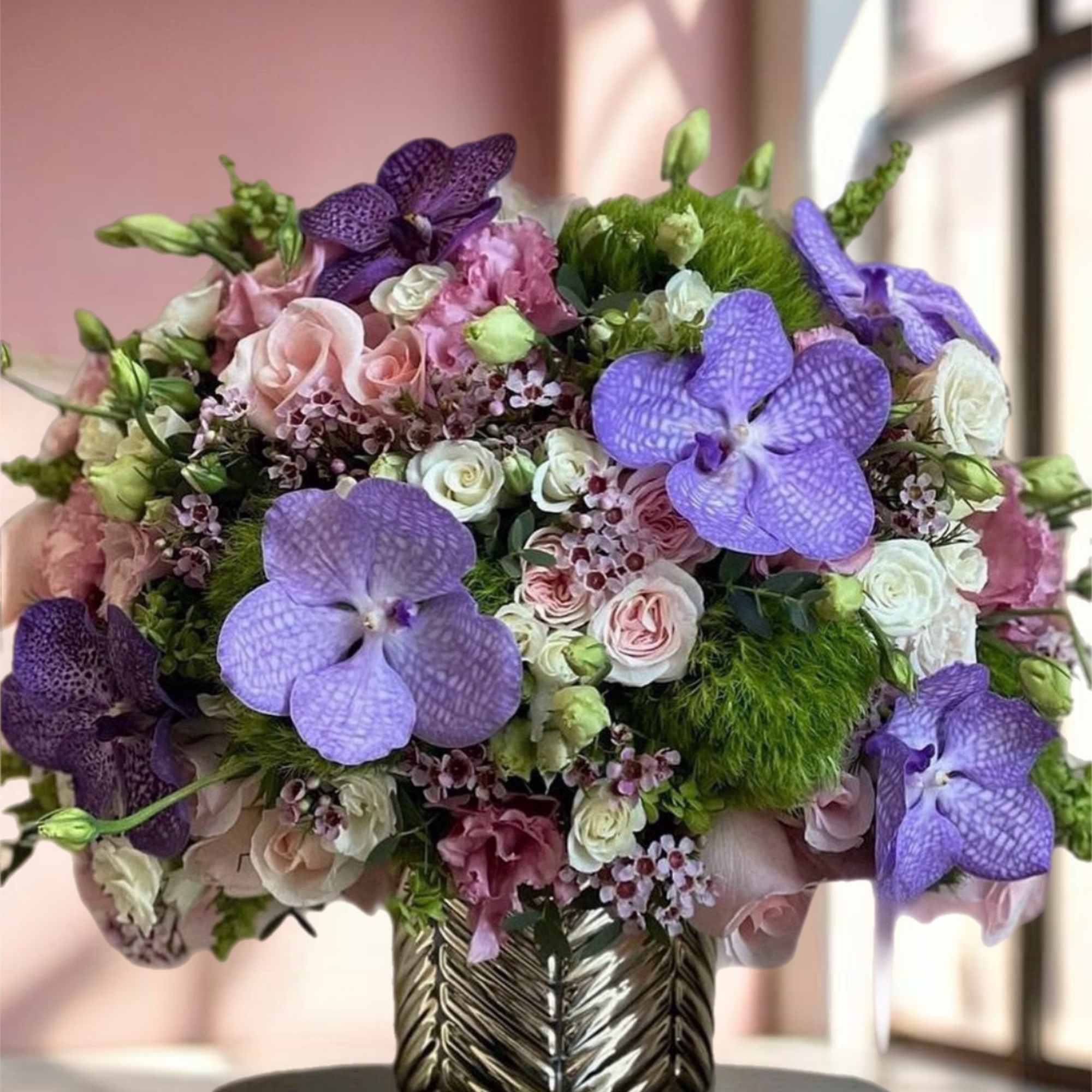 Purple orchids and pink roses arranged in a metallic vase
