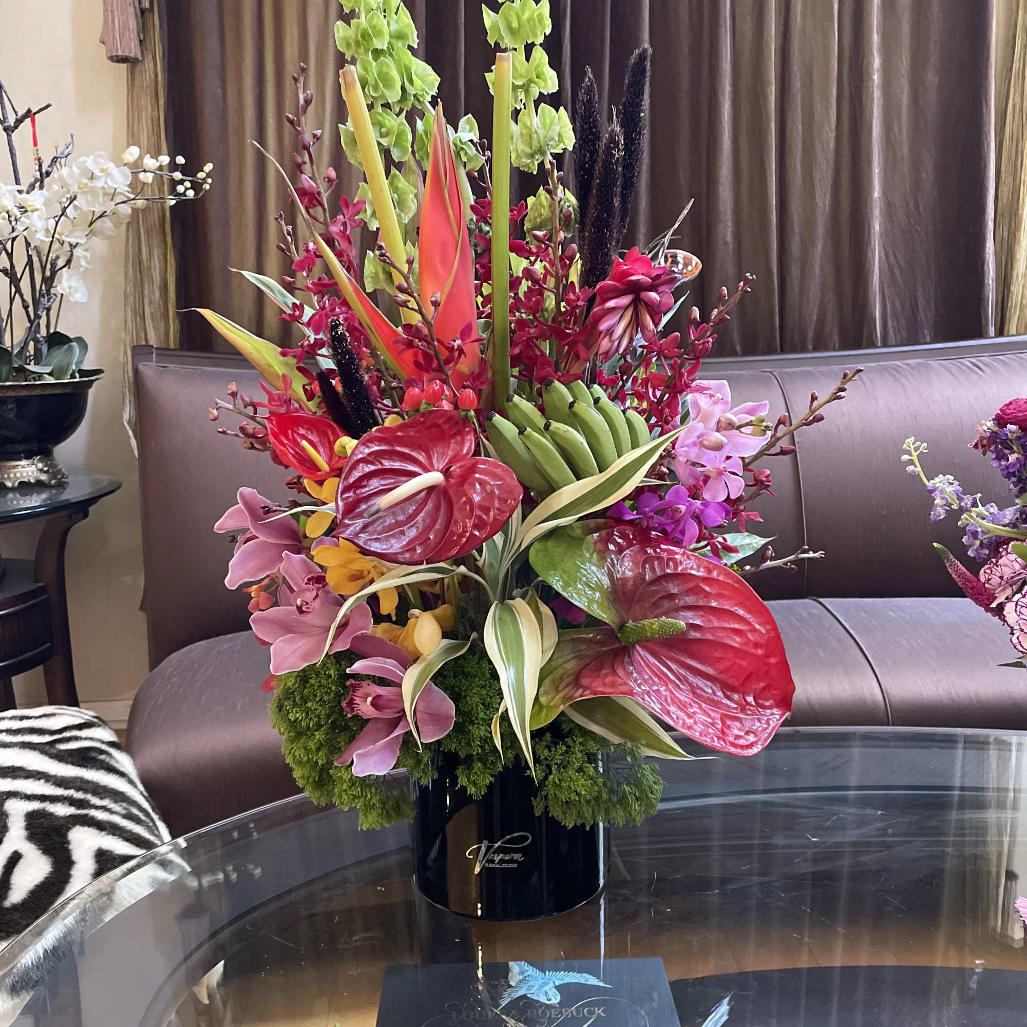 Tall tropical flower arrangement in a black vase with red anthuriums and pink orchids