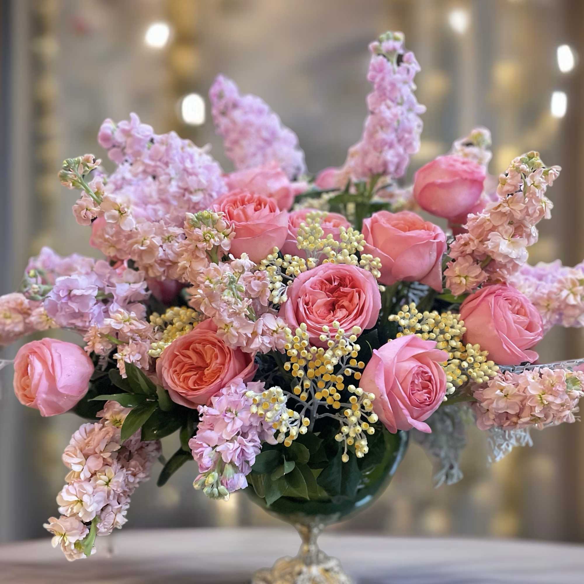 Pink roses and pale blossoms arranged in a glass pedestal vase