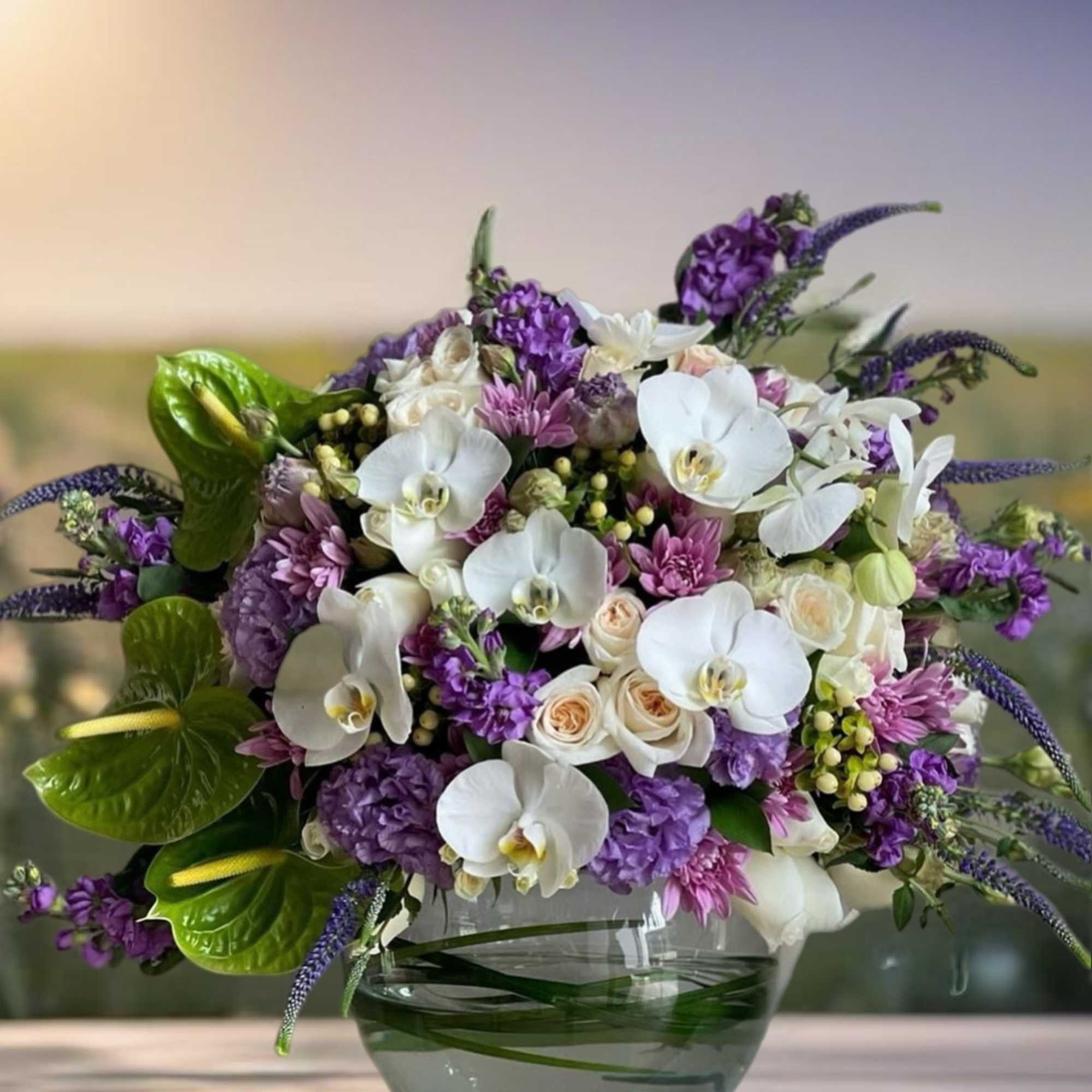 Purple and white floral arrangement in a glass bowl vase