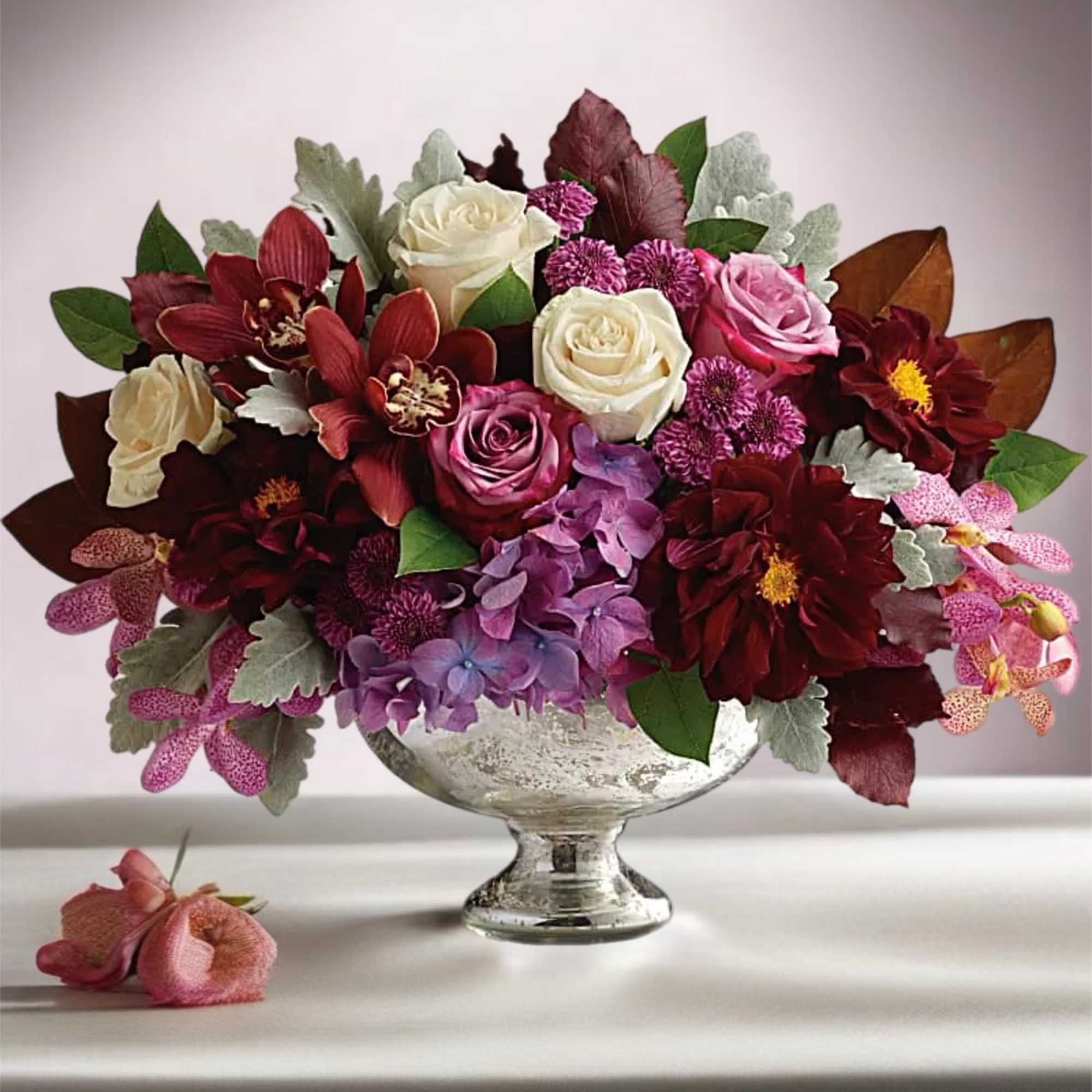 Mixed bouquet of roses, orchids, and purple blooms in a silver pedestal vase