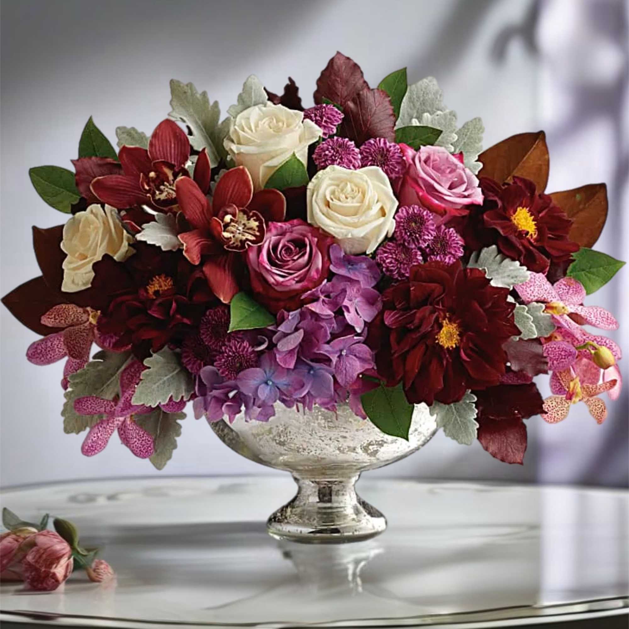 Mixed bouquet of roses, orchids, and hydrangeas in a silver pedestal vase
